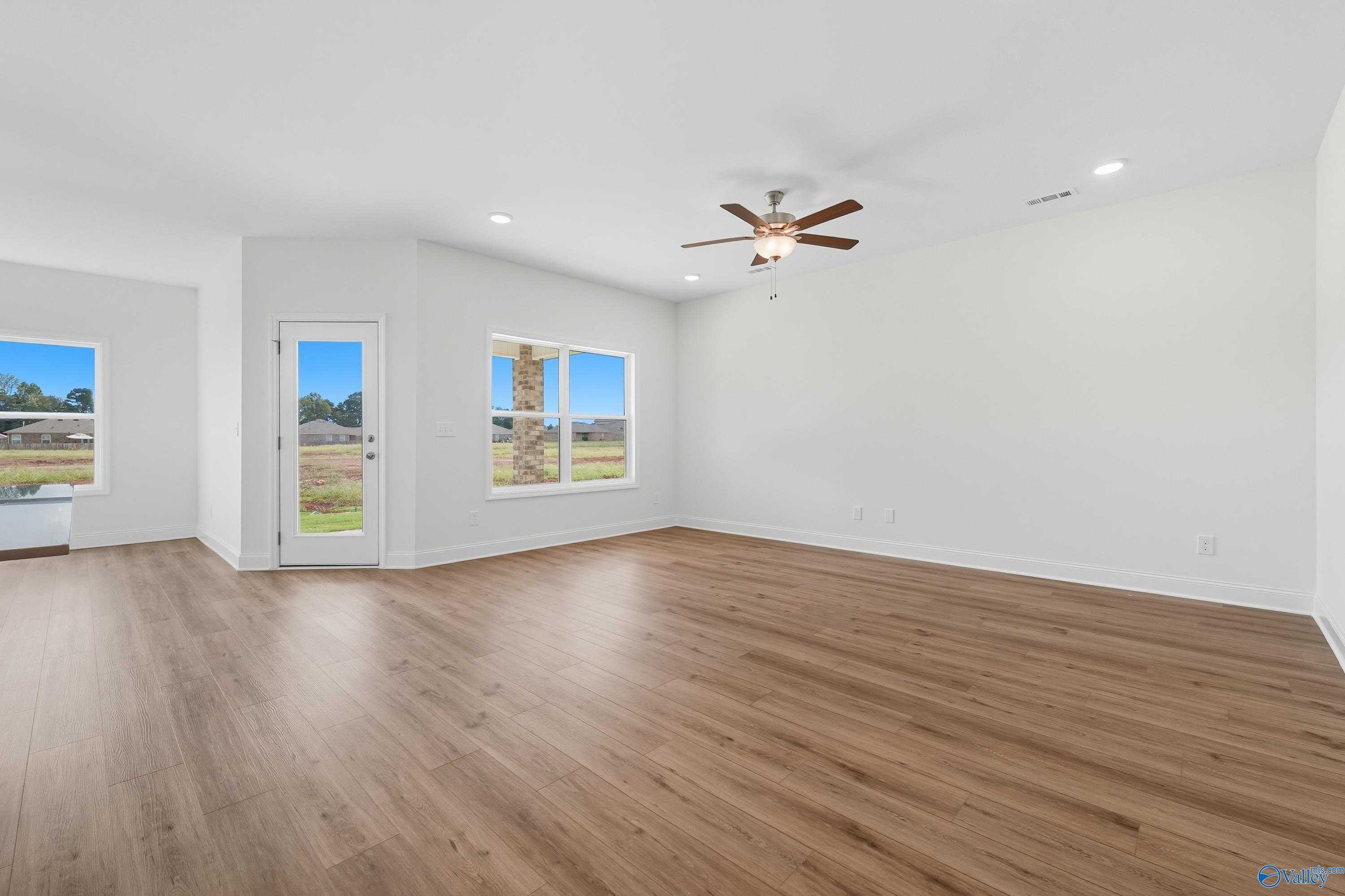 Bright living room with hardwood floors, ceiling fan, and large windows overlooking yard in The Everett home, Meridianville, AL