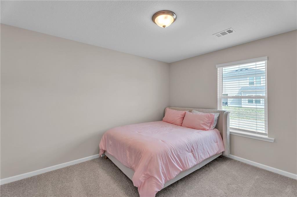 Cozy bedroom with pink bedding, beige walls, and window blinds in Davidson Homes The Bartlett, Phenix City, Alabama