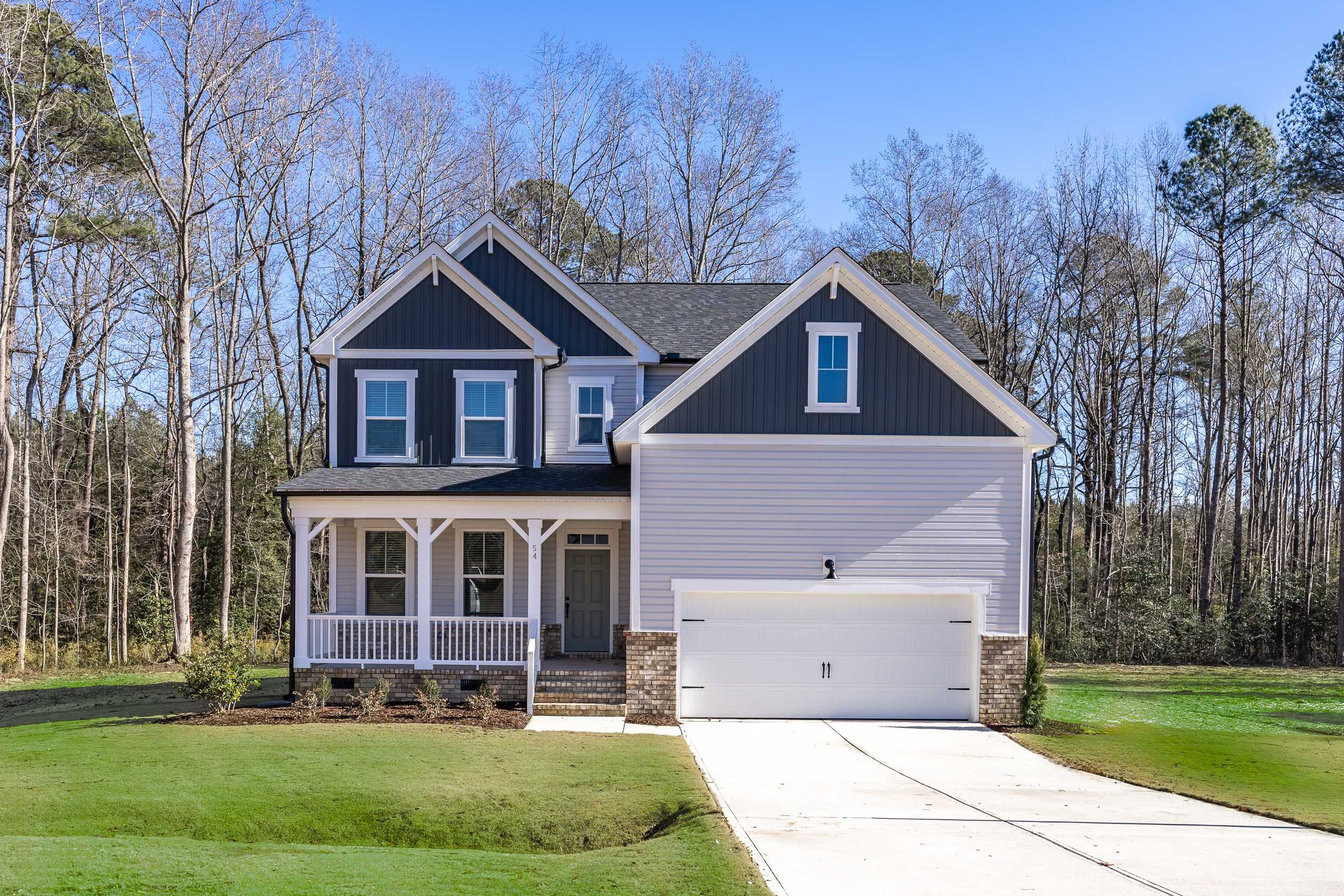 Two-story craftsman-style home exterior at Wellers Knoll in Lillington NC with covered porch, garage and wooded backdrop