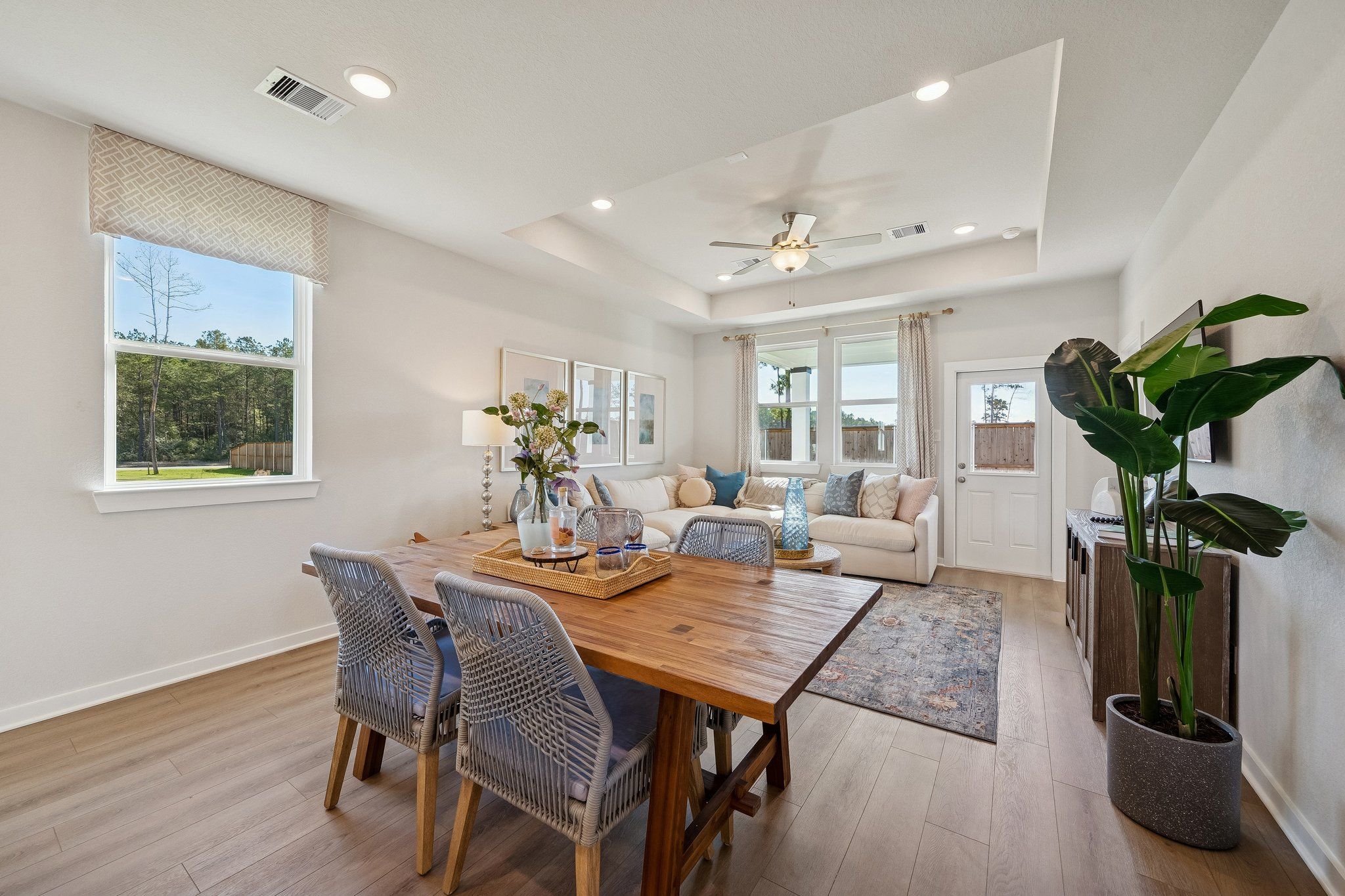 Open-concept dining and living room at Spring Branch Crossing in Conroe Texas with hardwood floors wooden table large windows and potted plants