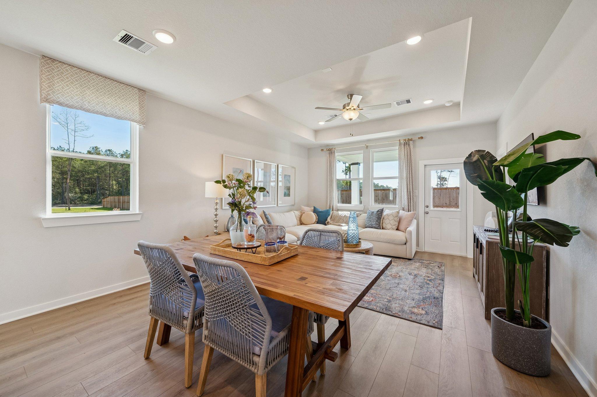 Open-concept dining and living room at Spring Branch Crossing in Conroe Texas with hardwood floors wooden table large windows and potted plants