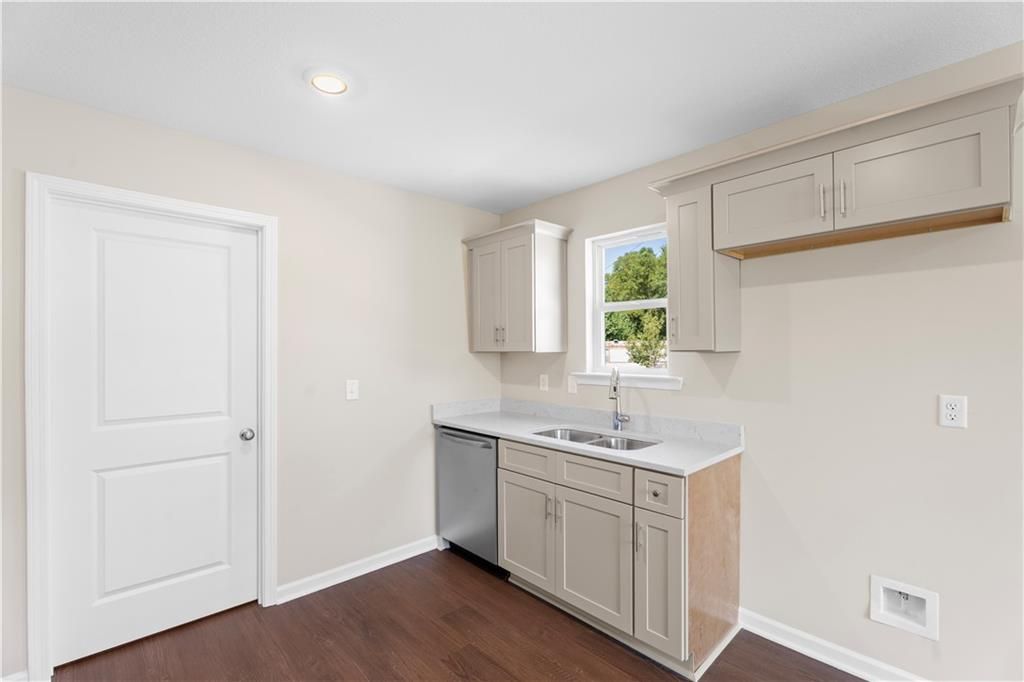 Modern beige kitchen with shaker cabinets, stainless dishwasher, white quartz counters, and tree-view window in Davidson Homes The Washington, Phenix City, AL
