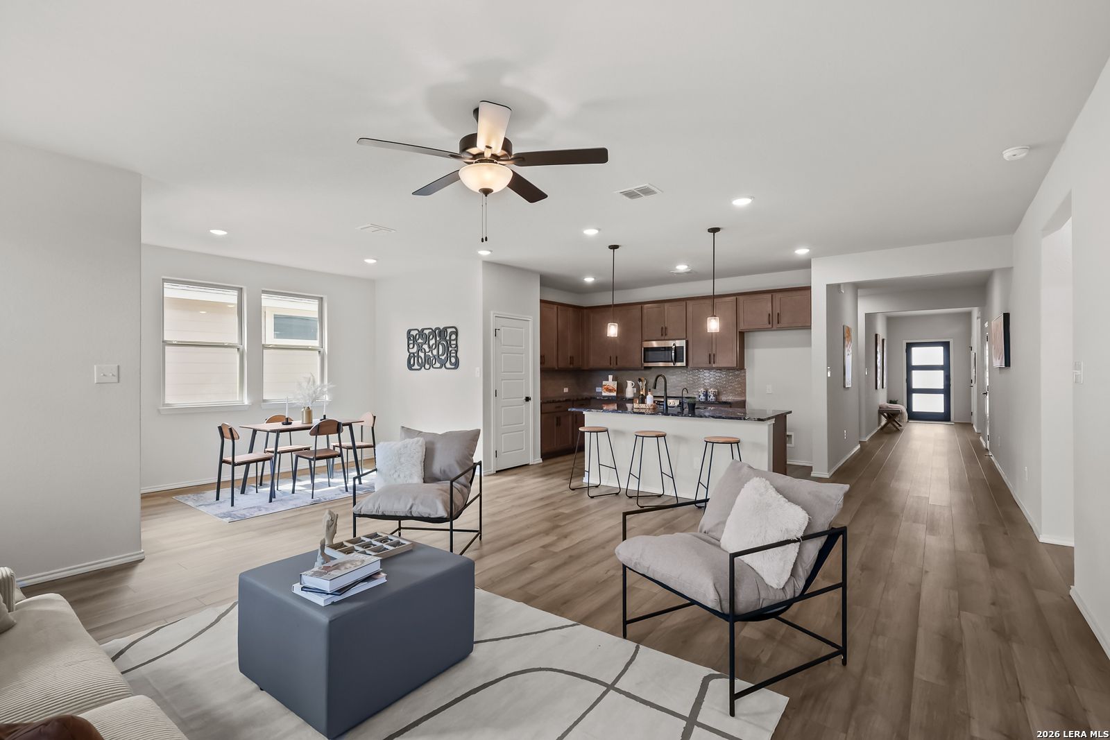 Open-concept living room and kitchen with wood floors, ceiling fan, bar island, and modern seating in The Daphne H, Seguin, Texas