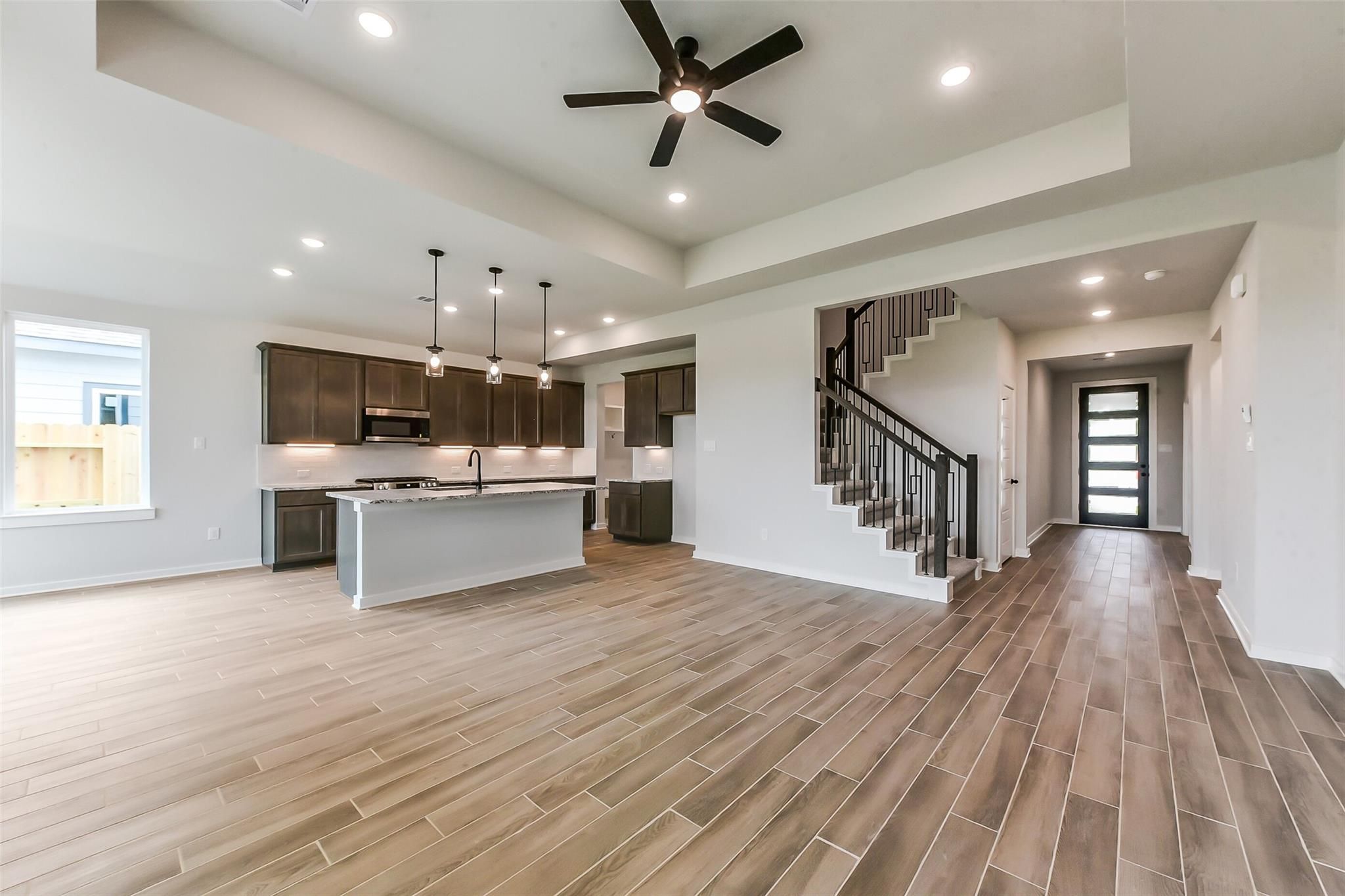 Open-concept kitchen with dark cabinets, white island, pendant lights, and staircase in Davidson Homes The Sequoia C, Crosby Texas