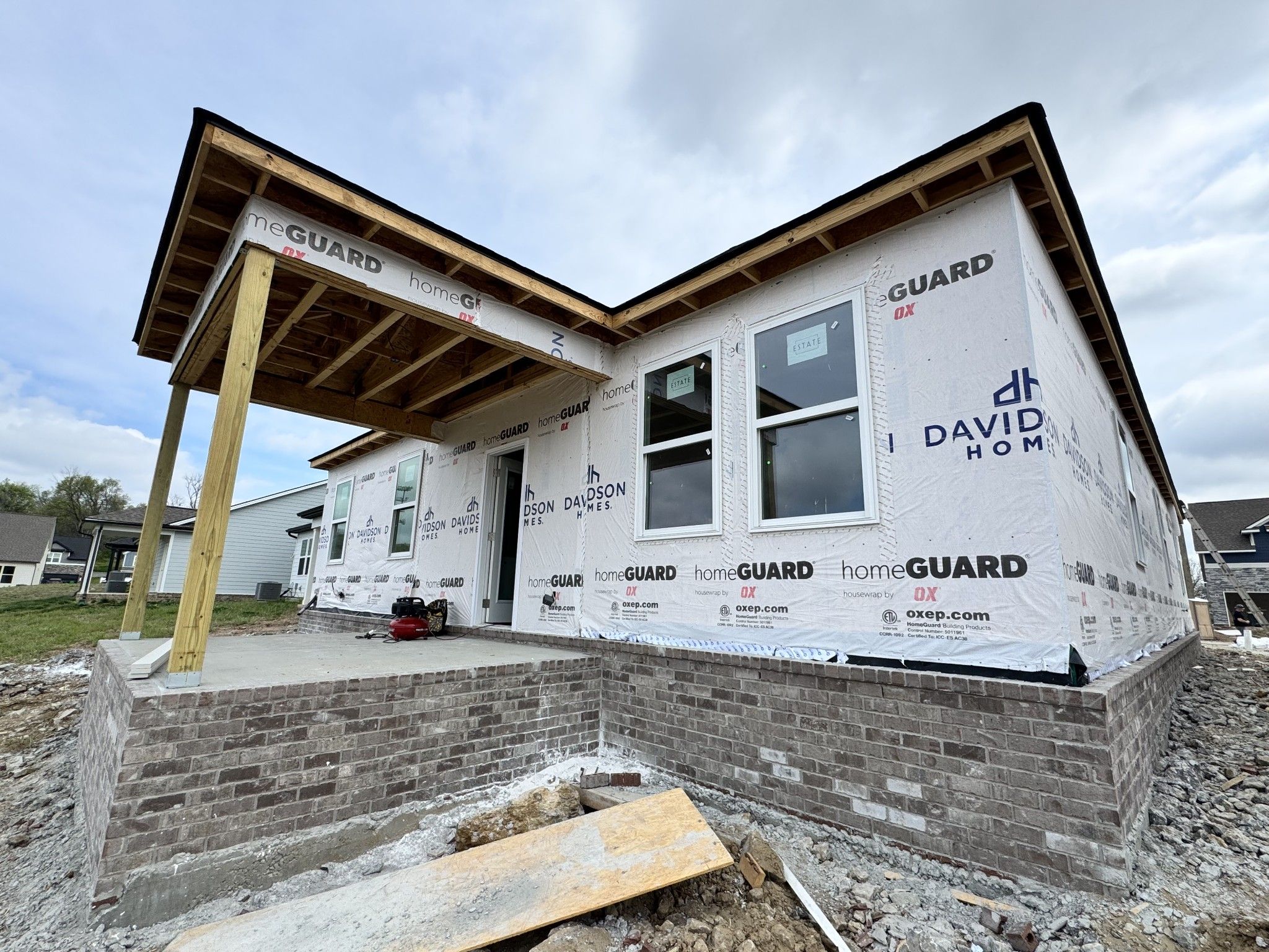 Under-construction front exterior of Davidson Homes The Cottonwood E in Woods Crossing, Gallatin, TN, with covered porch, windows, and brick base