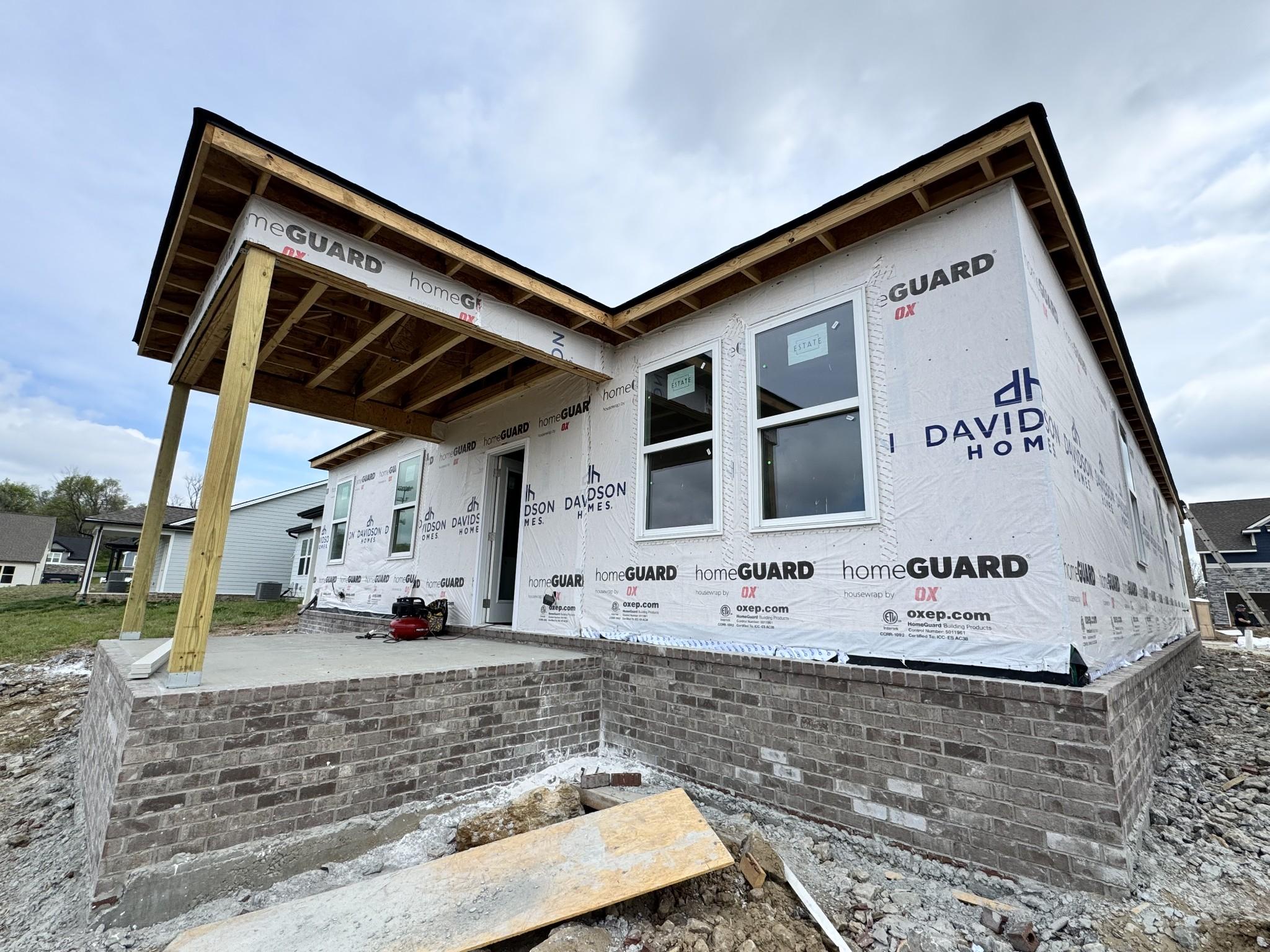 Under-construction front exterior of Davidson Homes The Cottonwood E in Woods Crossing, Gallatin, TN, with covered porch, windows, and brick base