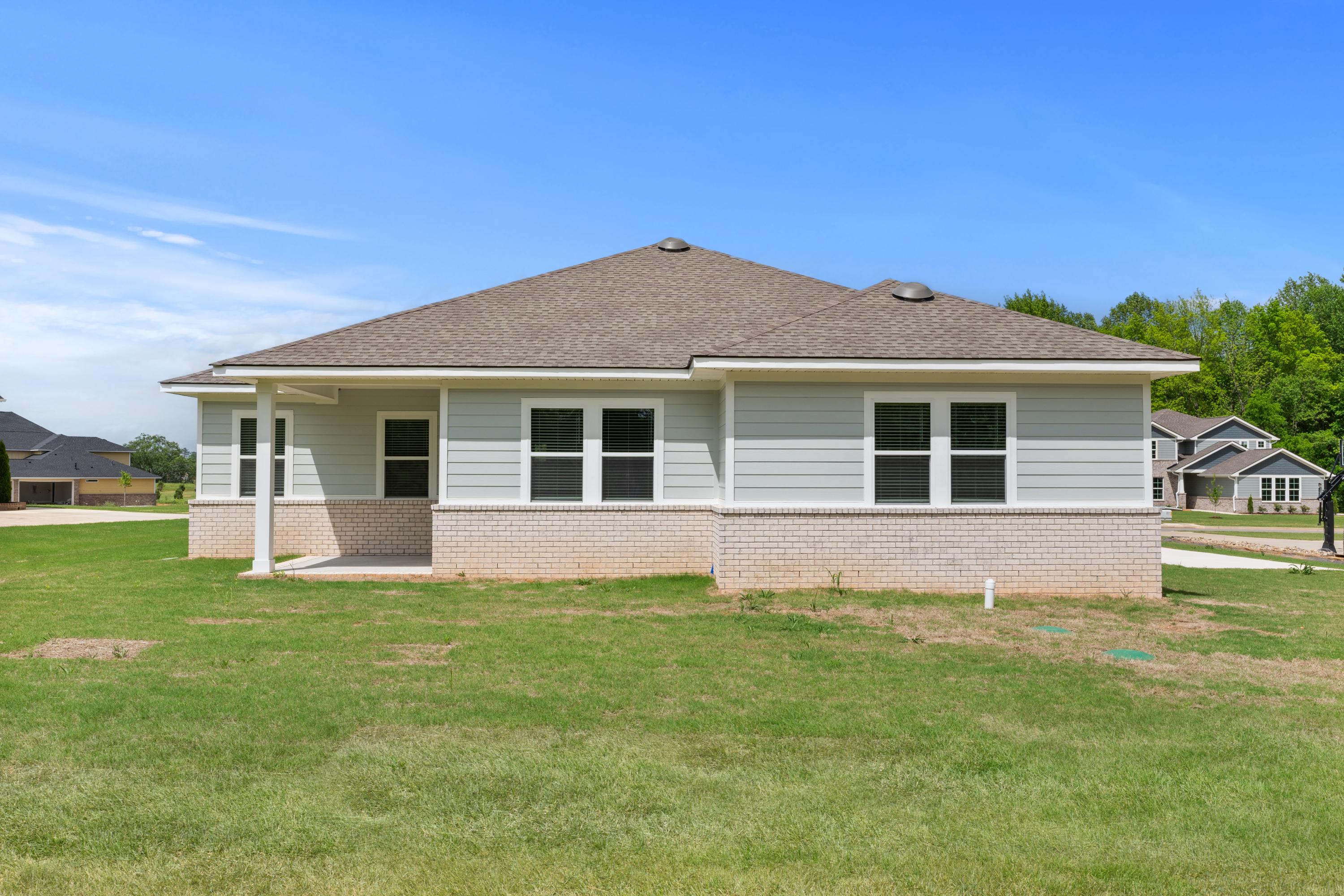 Single-story front elevation of The Arcadia B home featuring beige siding, brick foundation, covered porch, and double windows on grassy lot