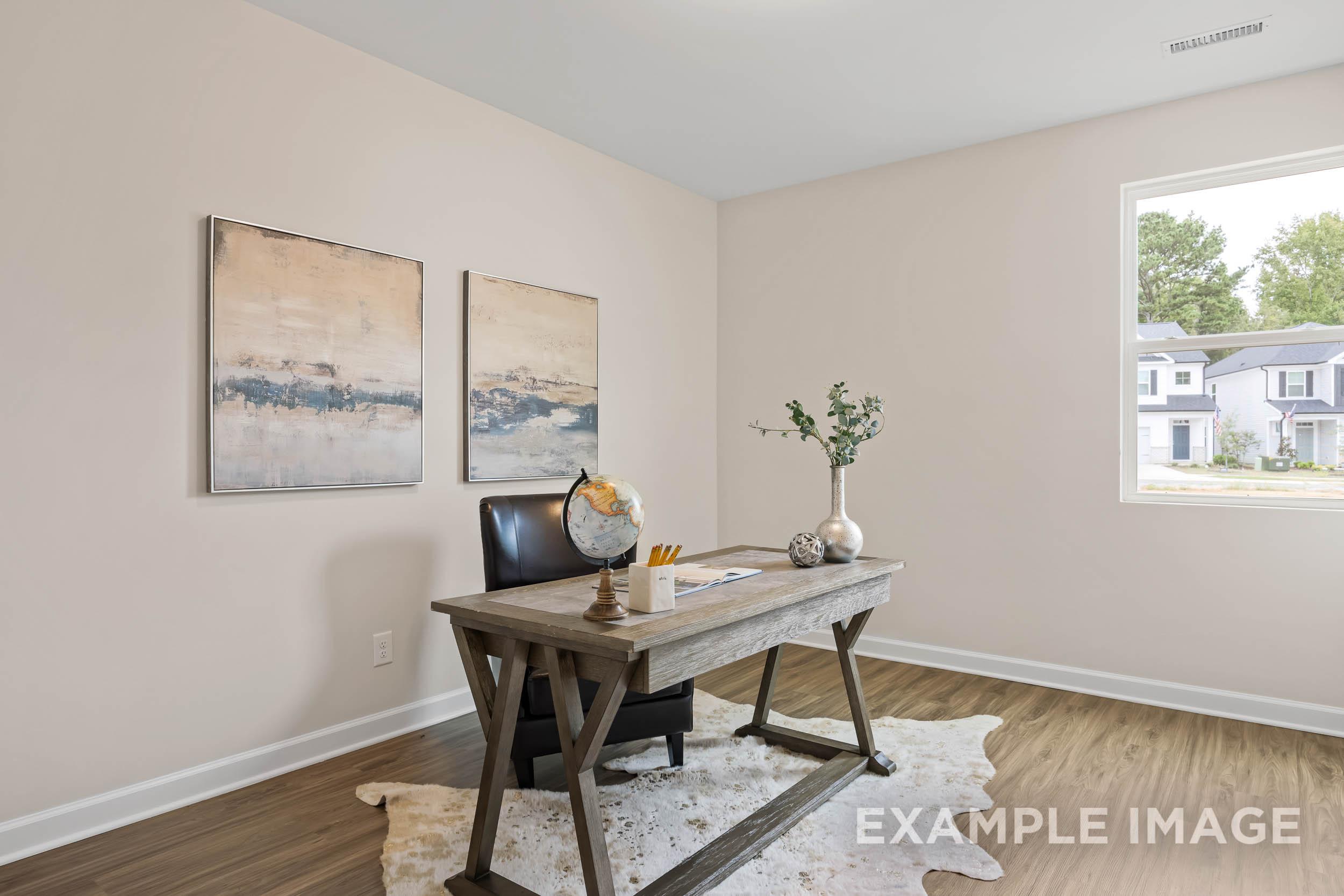 Cozy home office in The Preston B with rustic wooden desk, leather chair, abstract tan art, and tree-view window