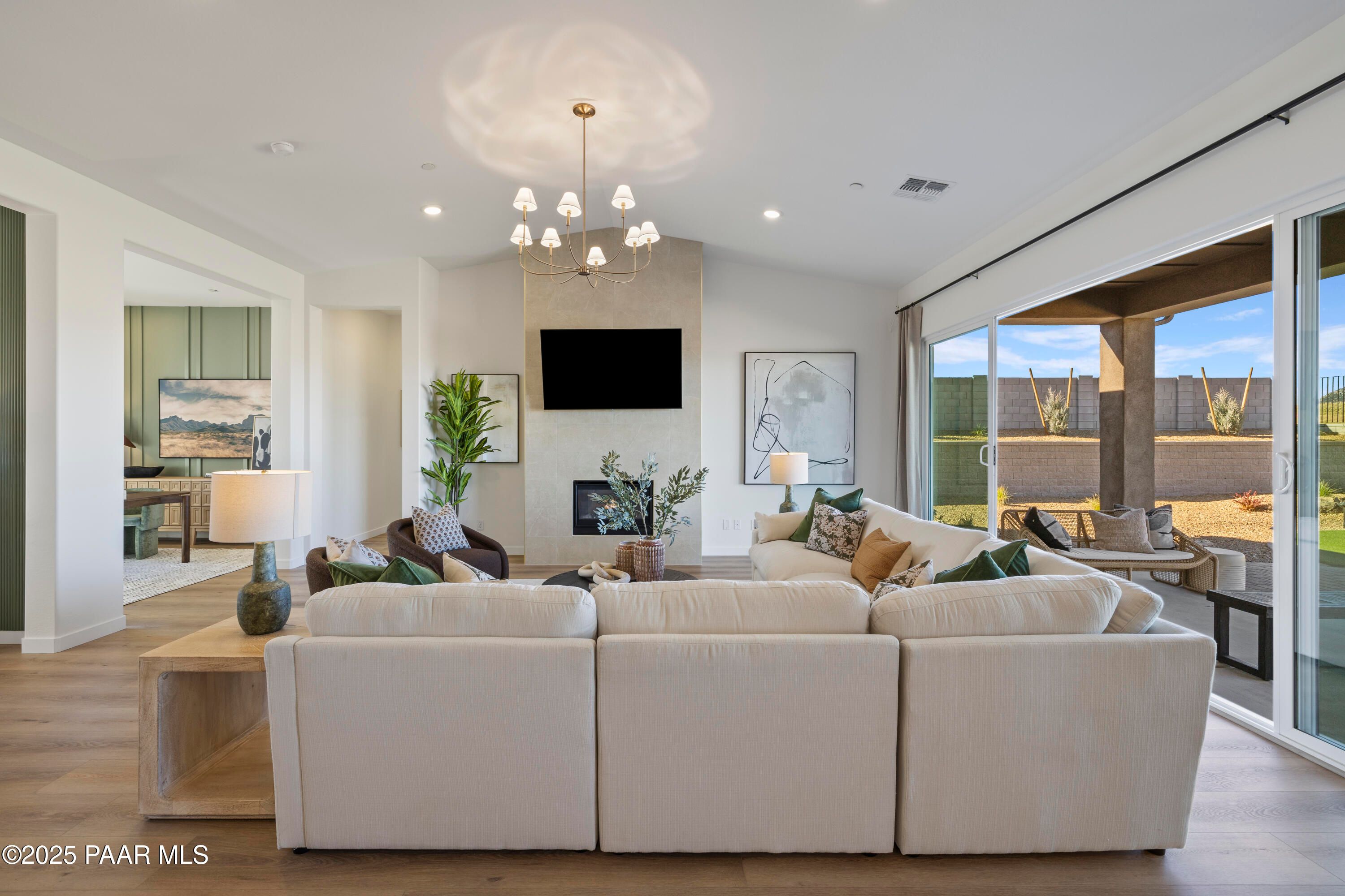 Cozy living room with white L-shaped sofa, fireplace, chandelier, and sliding doors to desert backyard in Davidson Homes The Blaze D, Prescott, AZ