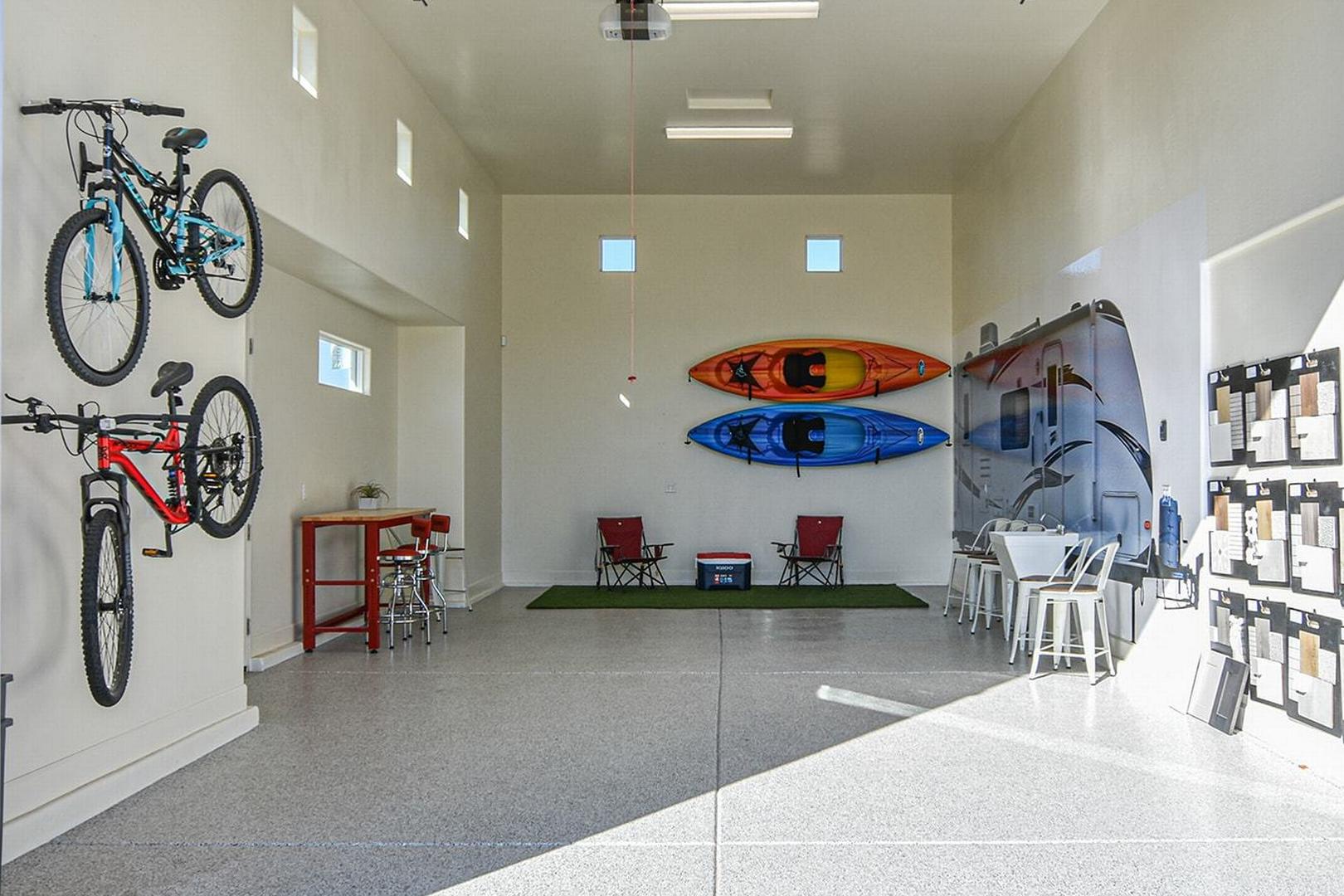 Spacious 3-car garage in The Summit E showcasing wall-mounted bikes, kayaks, trailer, and polished concrete floor by Evermore Homes