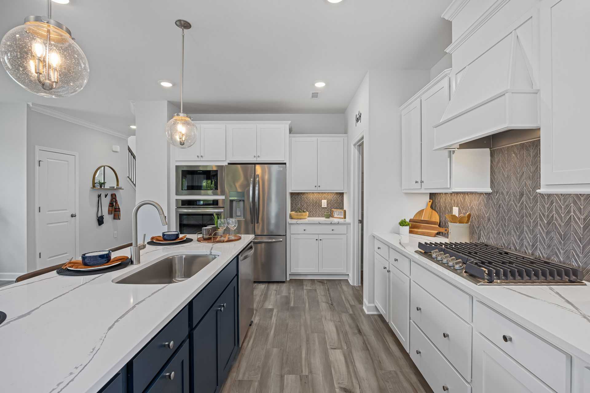 Spacious modern kitchen at Beverly Place in Four Oaks NC with white cabinets, navy island, quartz counters, herringbone backsplash