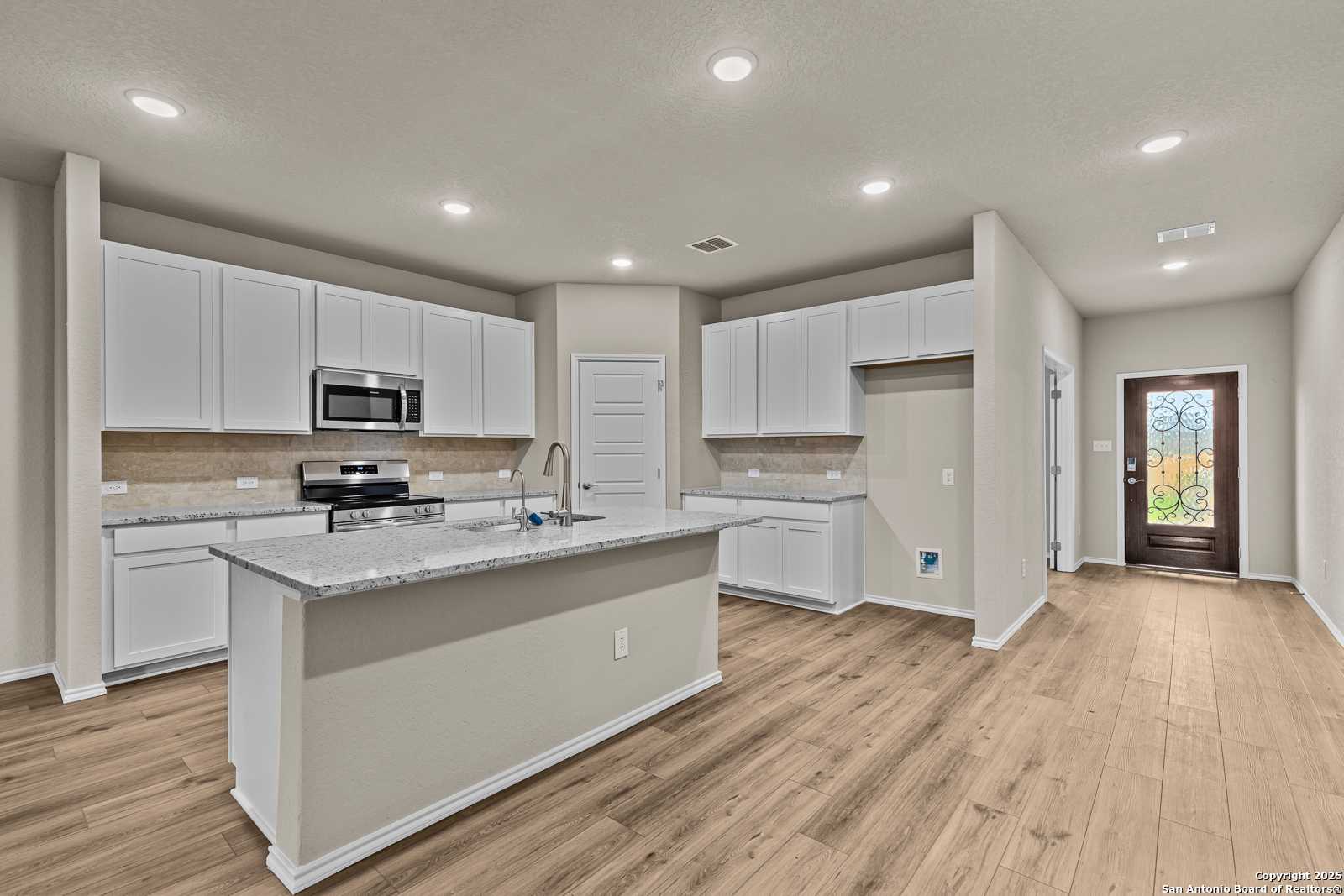 Modern kitchen with white cabinets, granite island, stainless appliances, hardwood floors in Davidson Homes The Douglas F, San Antonio