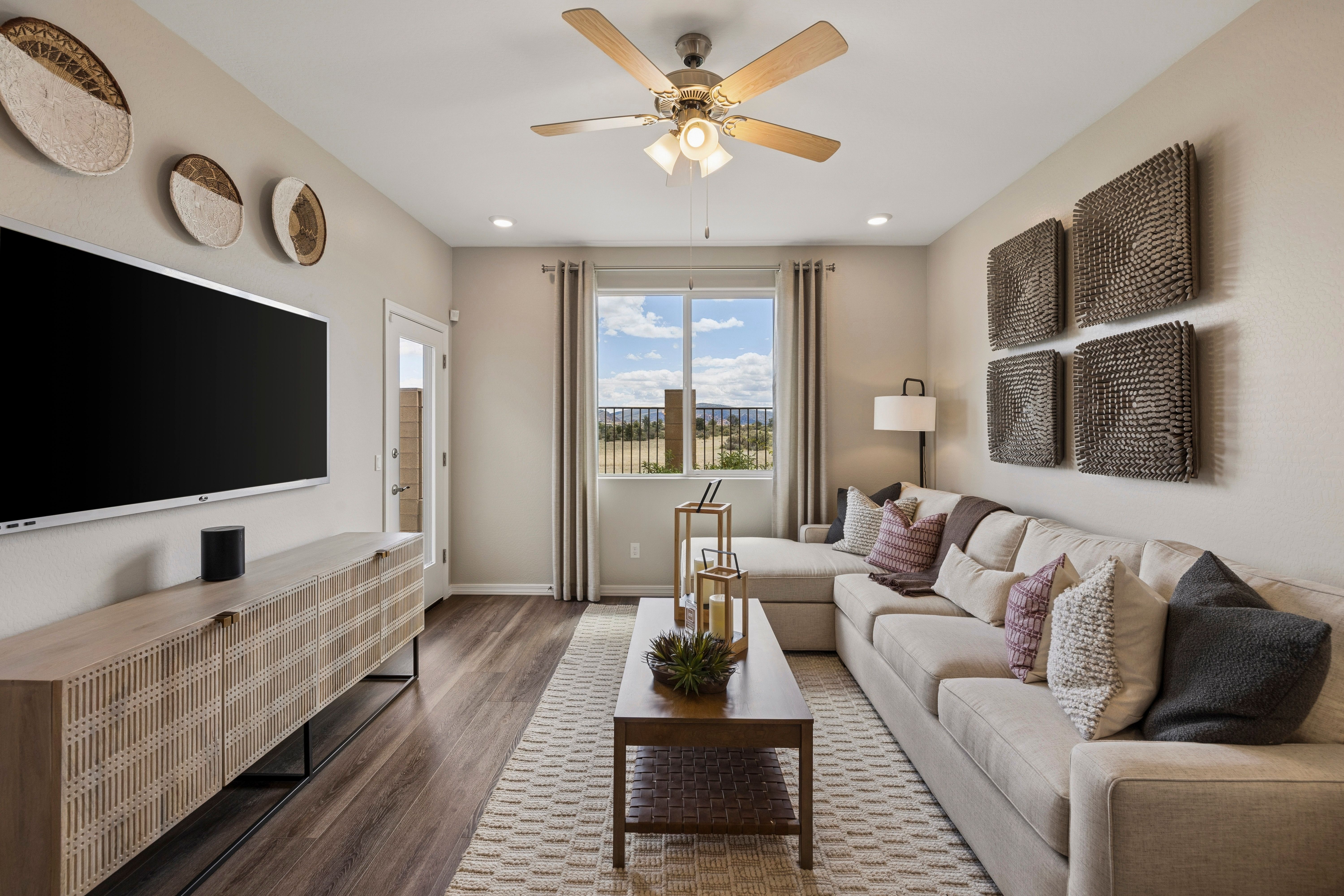 Cozy living room at Senator Cottages in Prescott AZ featuring L-shaped beige sofa, hardwood floors, woven wall art, and mountain view windows by Davidson Homes