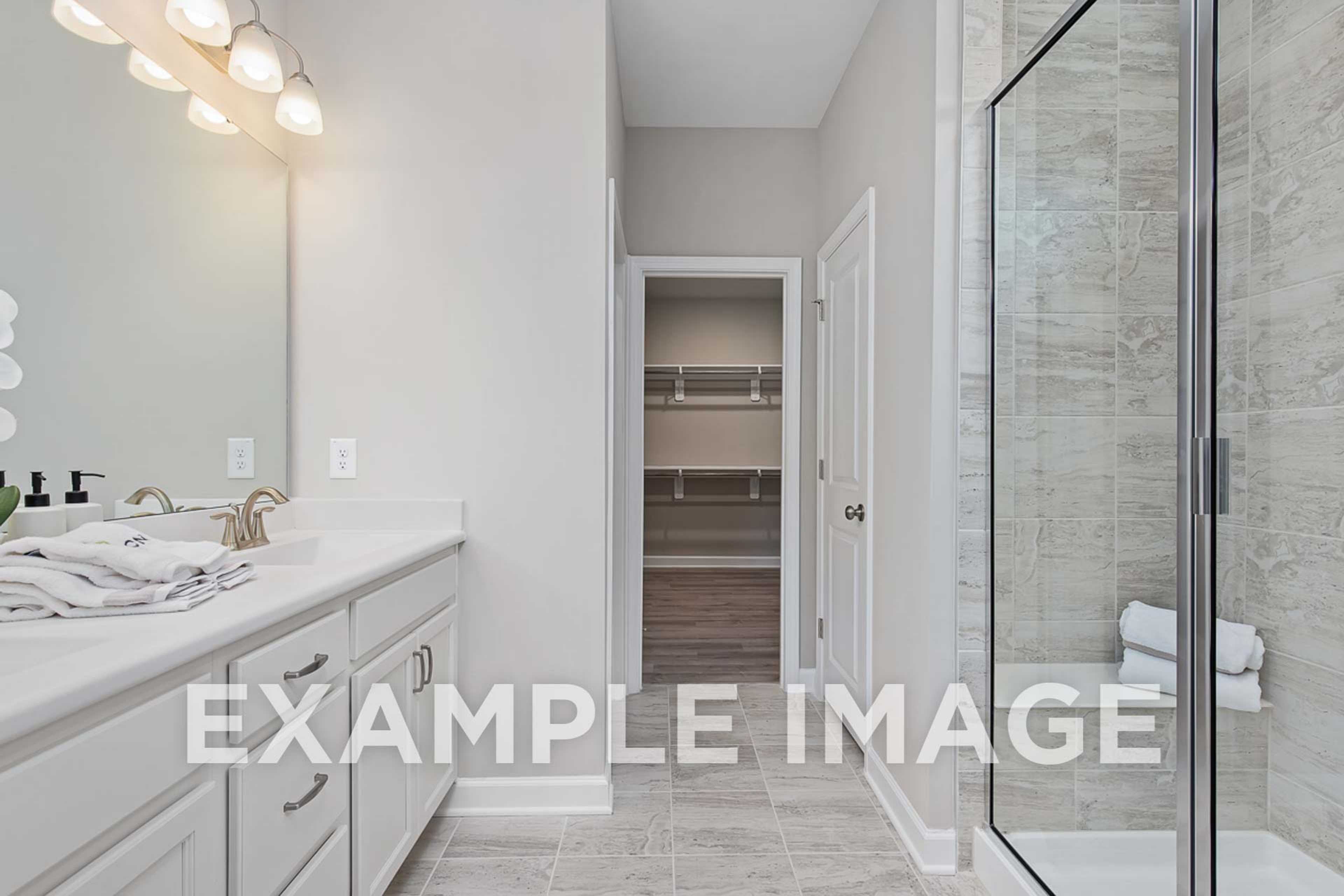 Spacious master bathroom in The Ash D featuring white vanity sink, frameless glass shower, and walk-in closet access