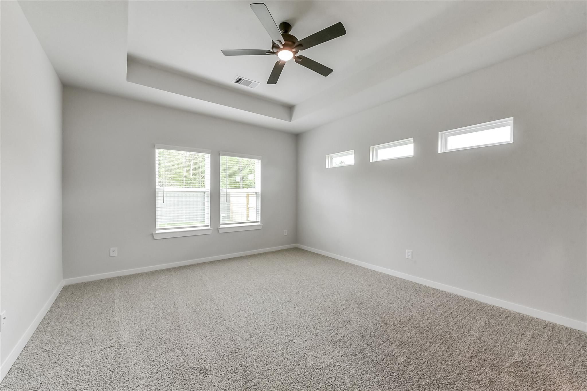 Bright bedroom with gray carpet, ceiling fan, large windows, and clerestory windows in Davidson Homes The Everett C, Crosby Texas