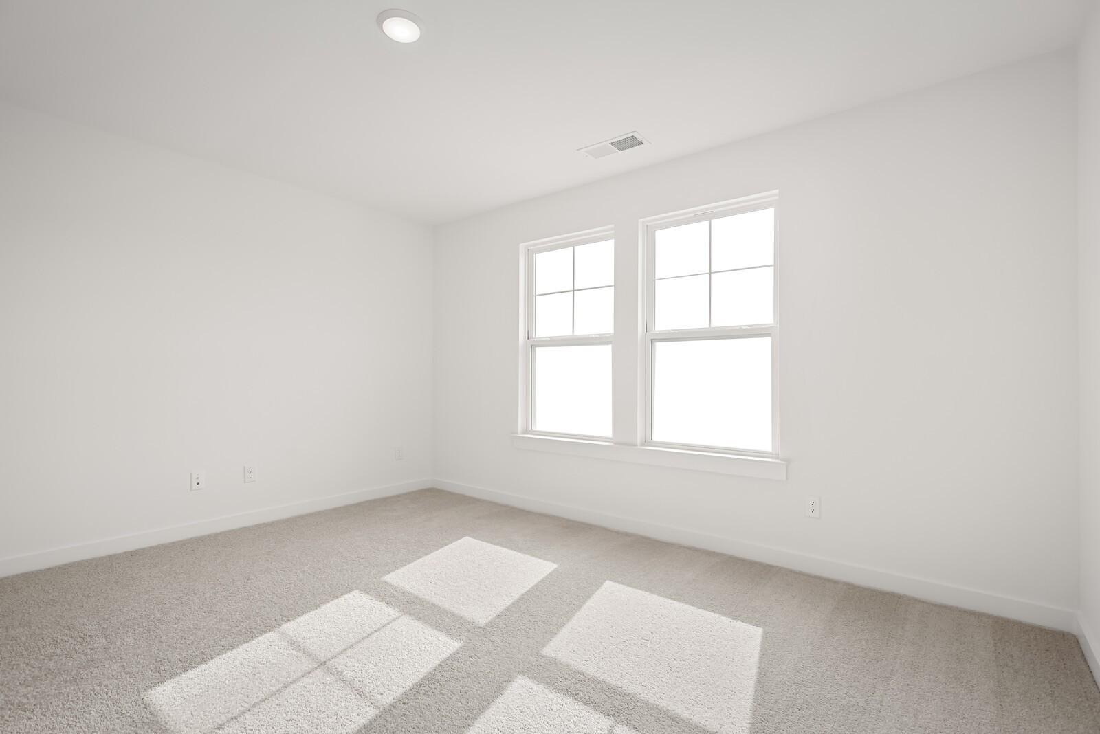 Bright empty bedroom with large windows, white walls, and beige carpet in Davidson Homes The Logan C, Gallatin, Tennessee
