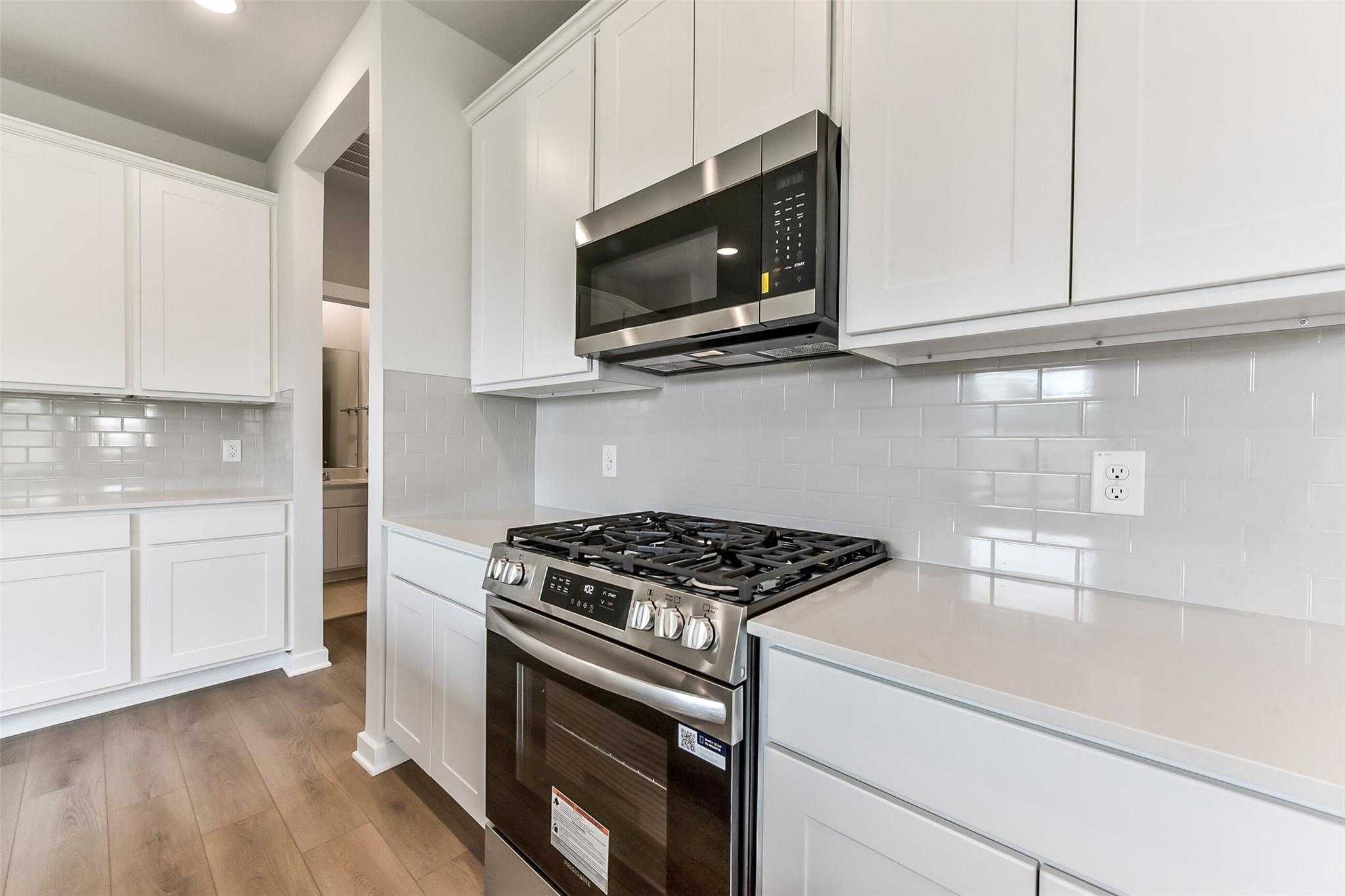 Modern kitchen with white shaker cabinets, stainless steel gas range, subway tile backsplash in Davidson Homes The Frio F, Dayton, Texas