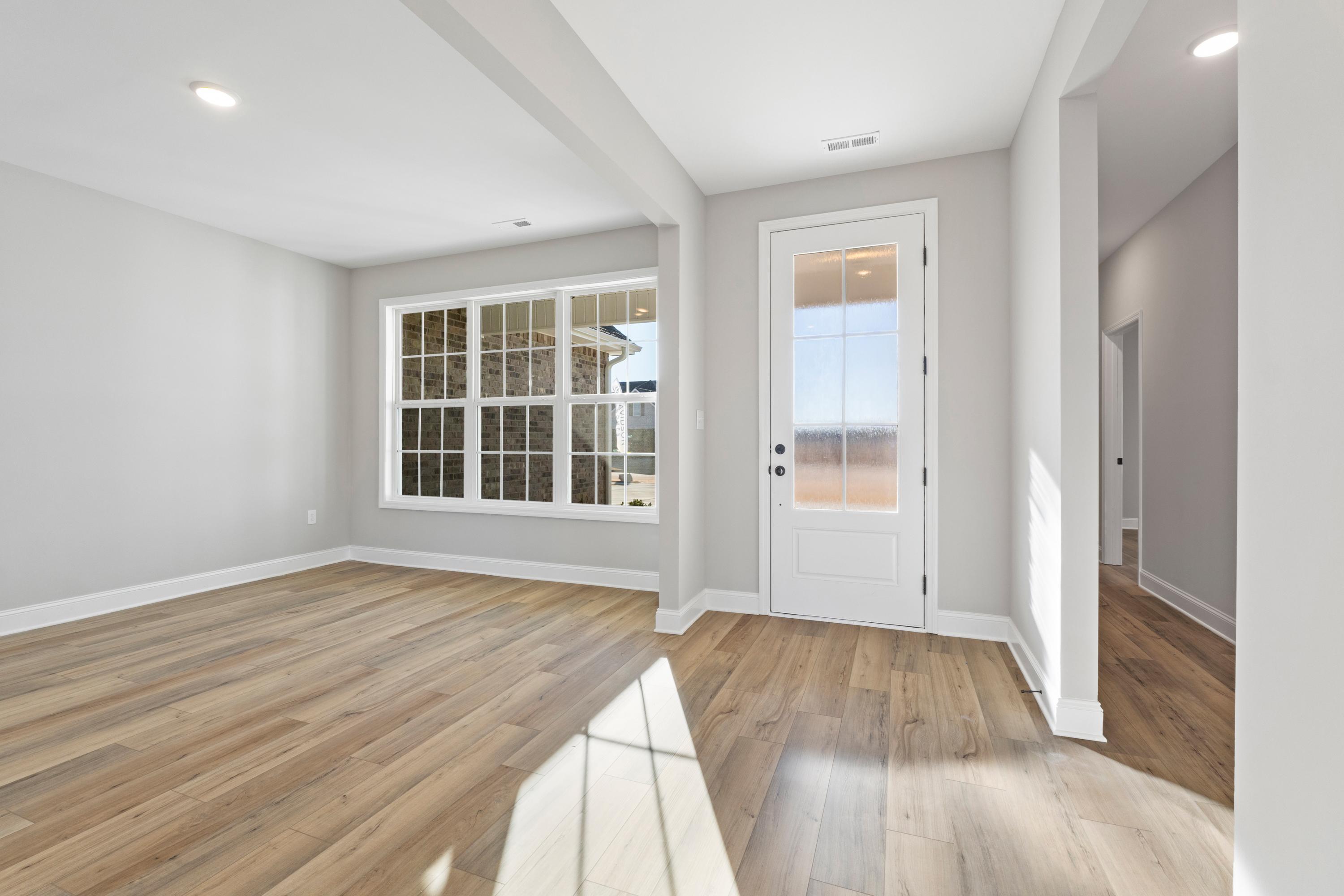 Bright great room in The Valencia with light hardwood floors, large windows, and glass door to backyard patio