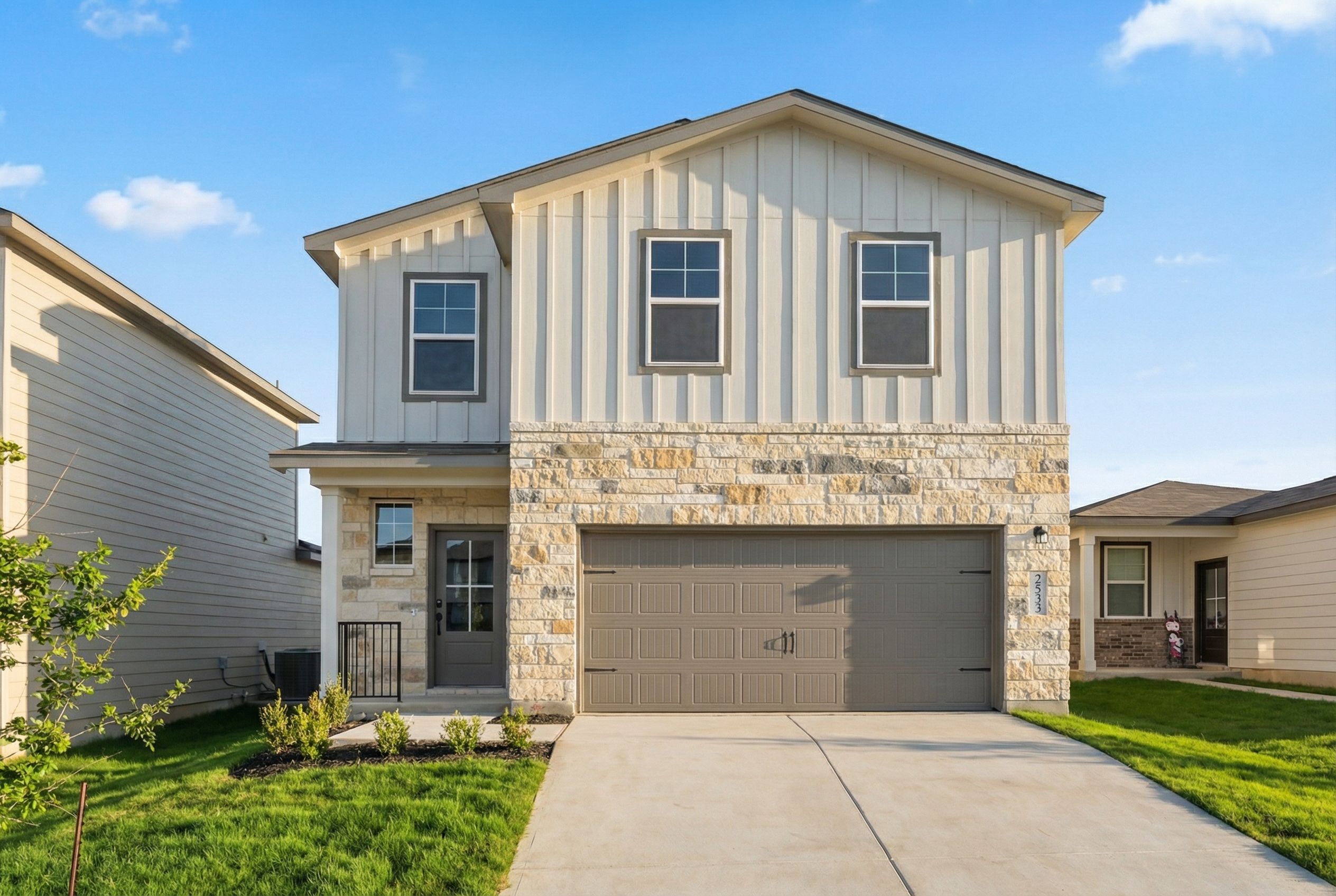 Modern stone-accented home exterior at Morgan Meadows in San Antonio TX with covered porch, two-car garage, and lush lawn