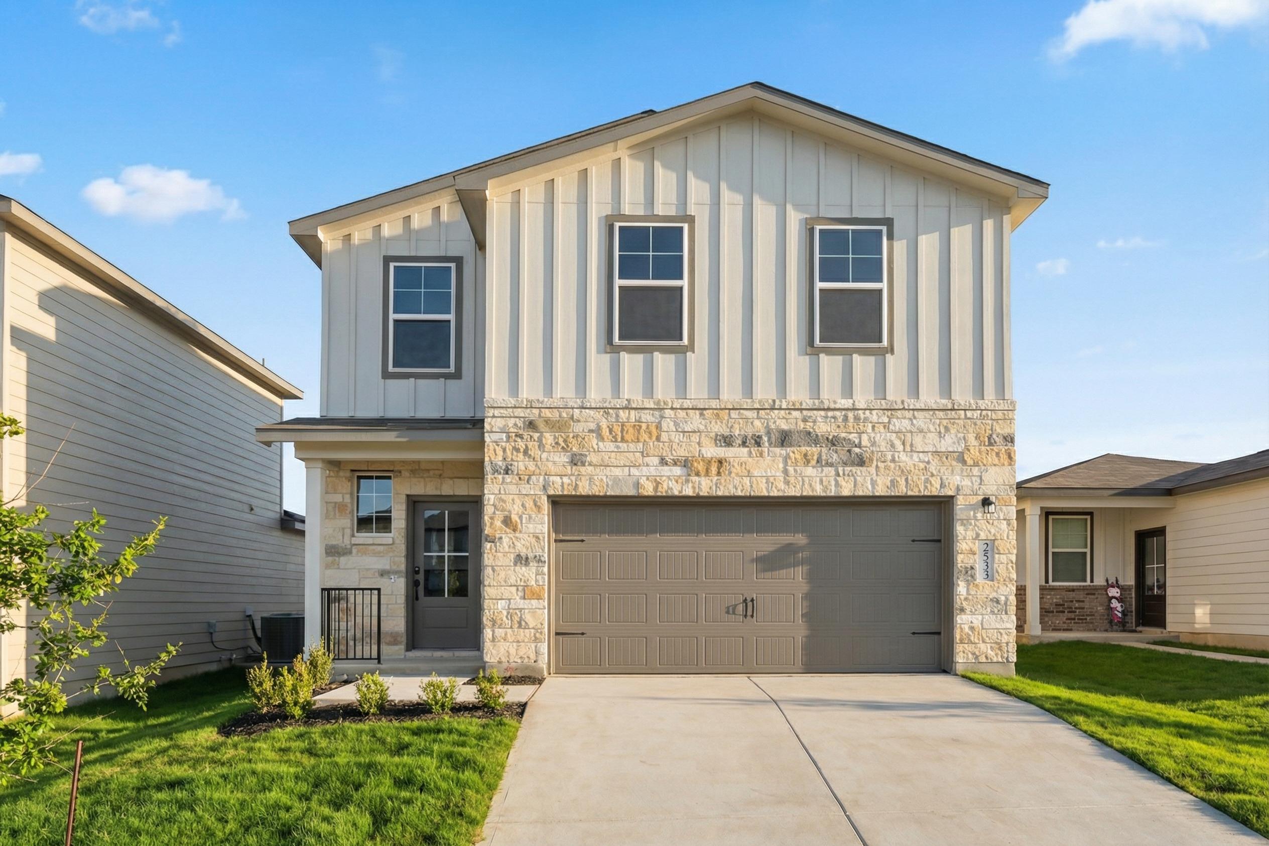 Modern stone-accented home exterior at Morgan Meadows in San Antonio TX with covered porch, two-car garage, and lush lawn
