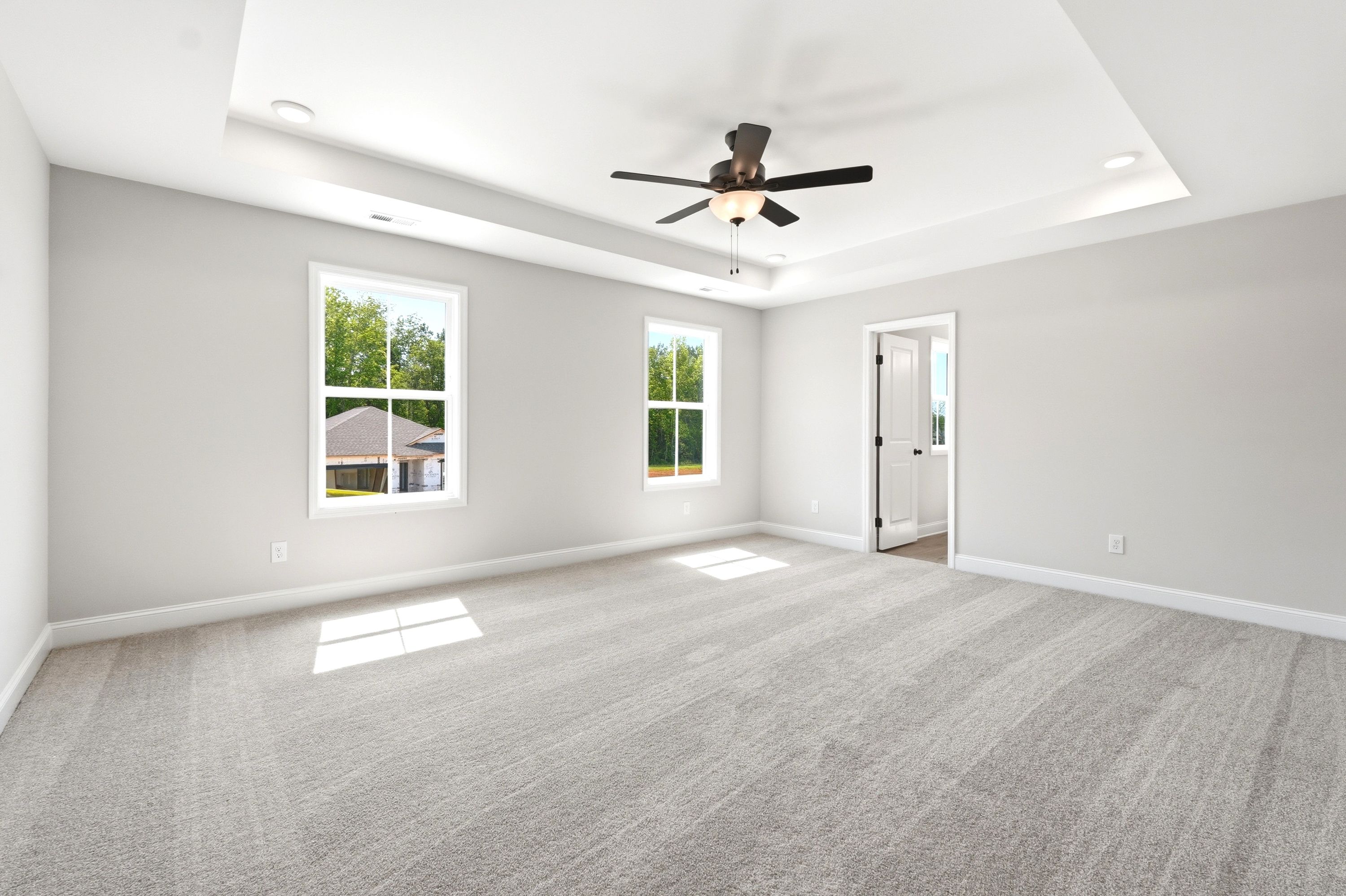 Spacious master suite with tray ceiling, carpeted flooring, and ceiling fan in The Russell A home design.