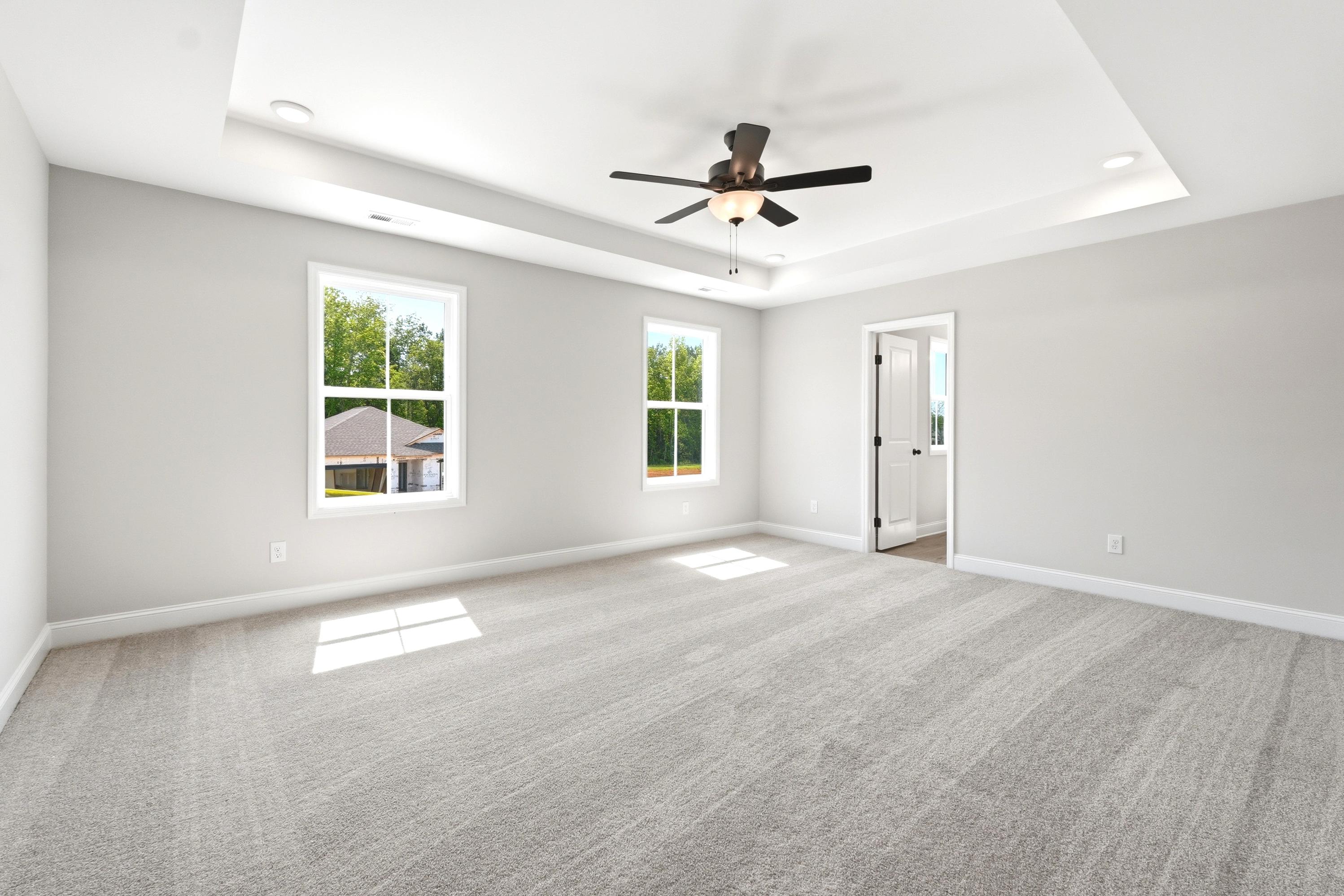 Spacious master suite with tray ceiling, carpeted flooring, and ceiling fan in The Russell A home design.