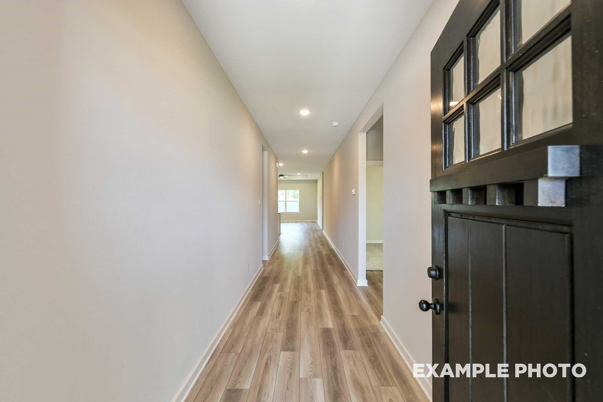 Spacious hallway with beige walls, hardwood floors, and glass-paneled front door in 4-bedroom Davidson Homes Everett C, Crosby, Texas