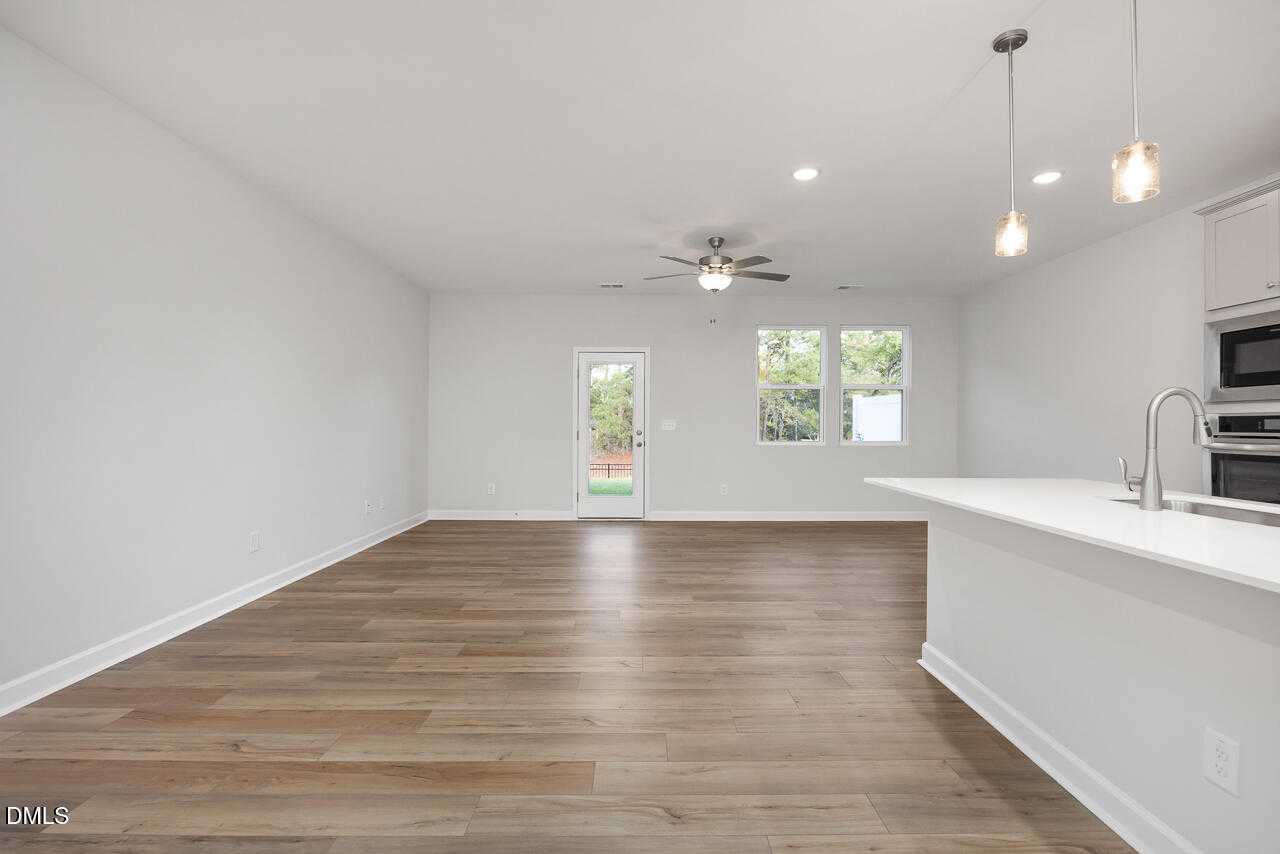 Open-concept living and kitchen with white cabinets, stainless appliances, ceiling fan, and backyard view in Davidson Homes The Warren, Fuquay-Varina