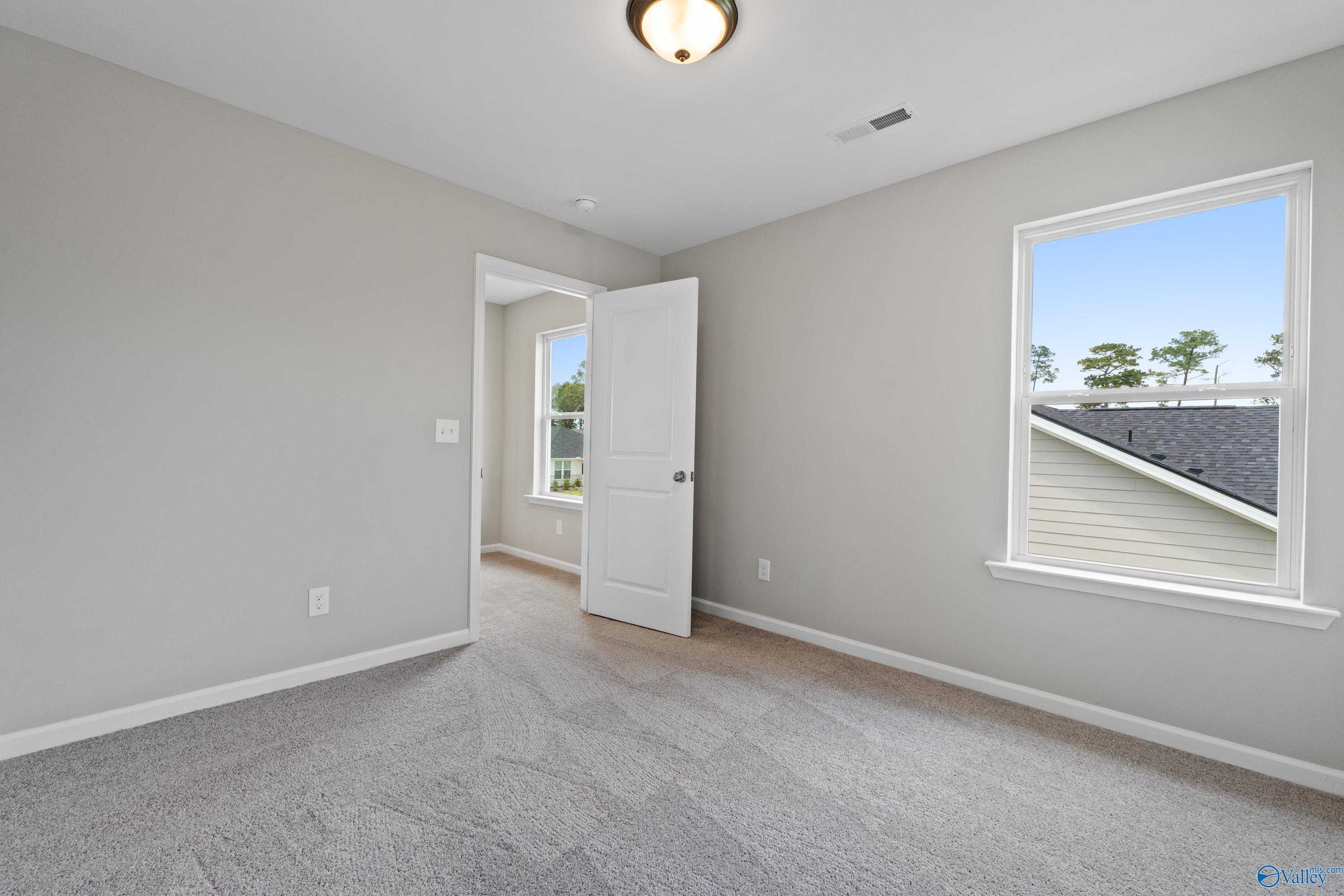 Bright empty bedroom with gray walls, carpet flooring, and window view in The Augusta plan, Madison, Alabama