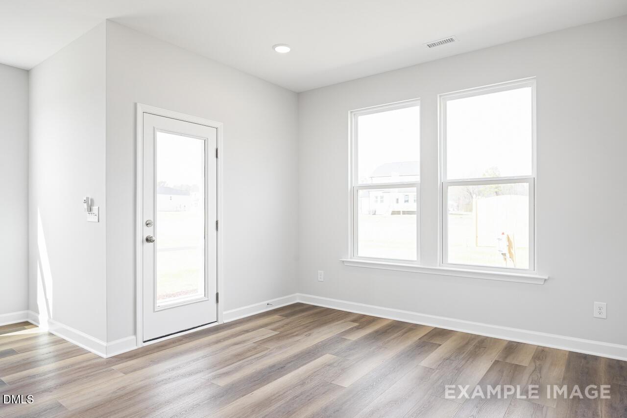 Bright bedroom with white walls, large windows, glass-paneled door, and luxury vinyl plank flooring in The Daphne C, Zebulon, NC