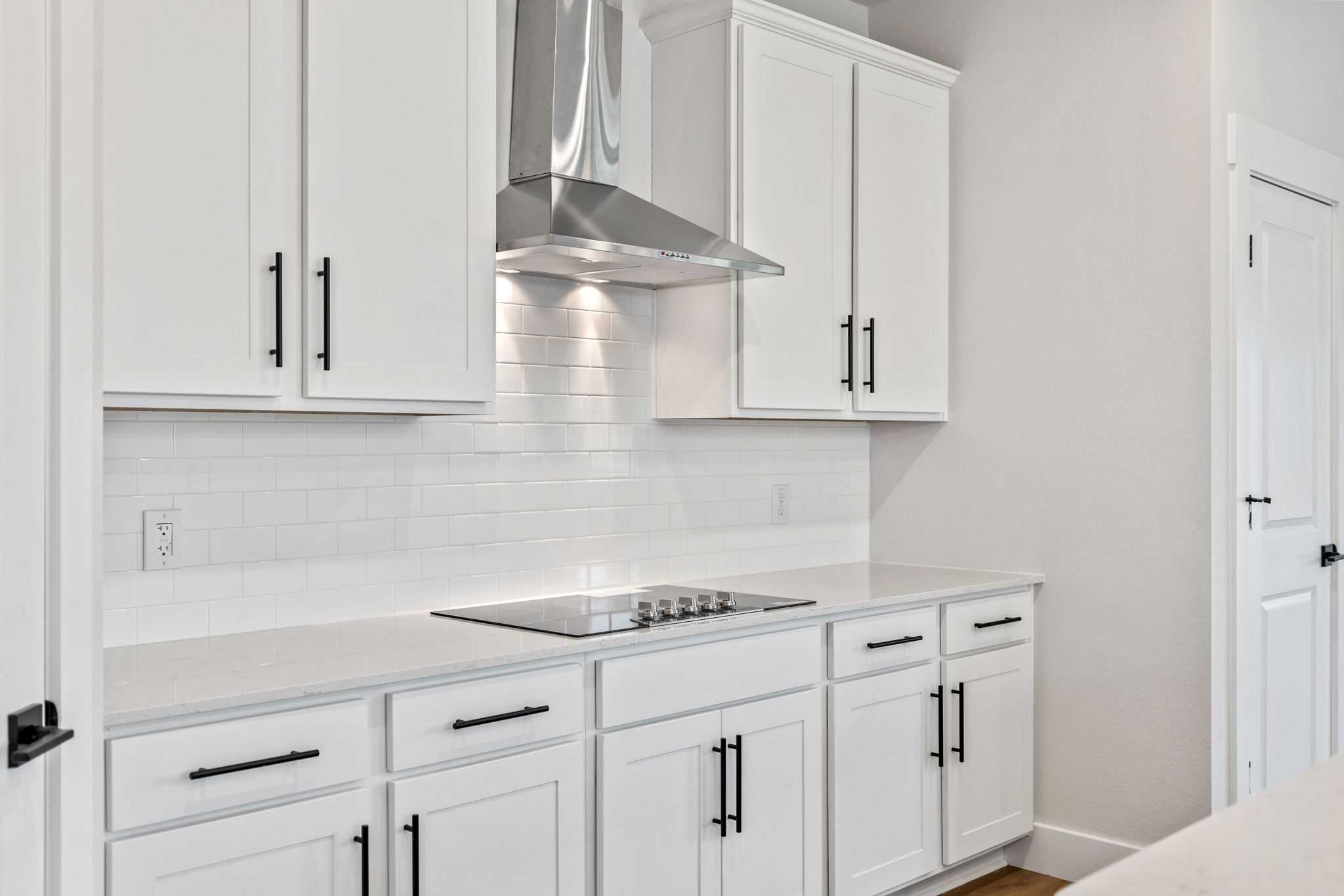 Modern white shaker kitchen with subway tile backsplash, stainless range hood, and induction cooktop in Davidson Homes The Durham E, Wylie, Texas