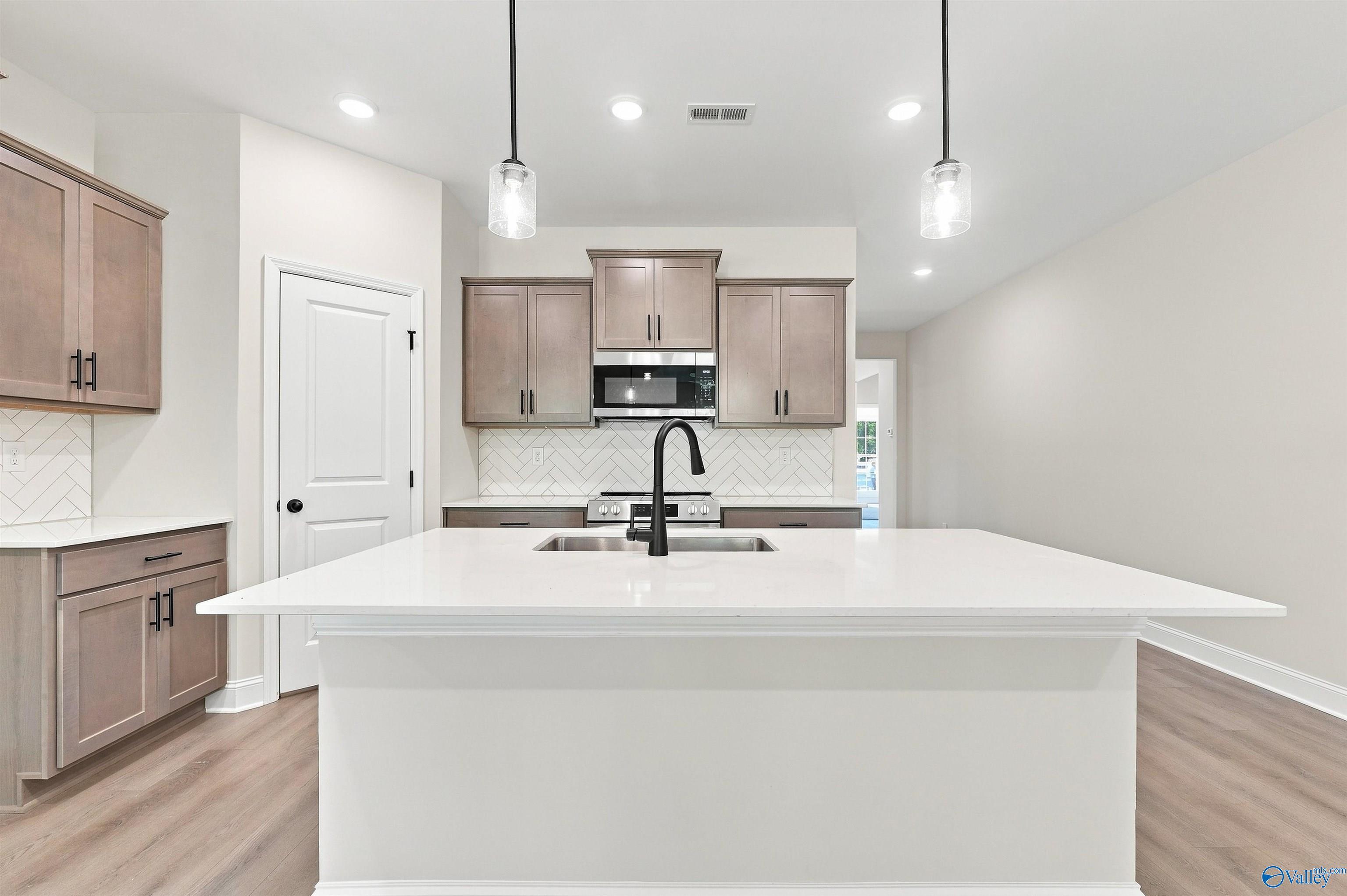 Modern kitchen with white island, quartz countertops, and herringbone backsplash in The Daphne floor plan, Huntsville, AL.