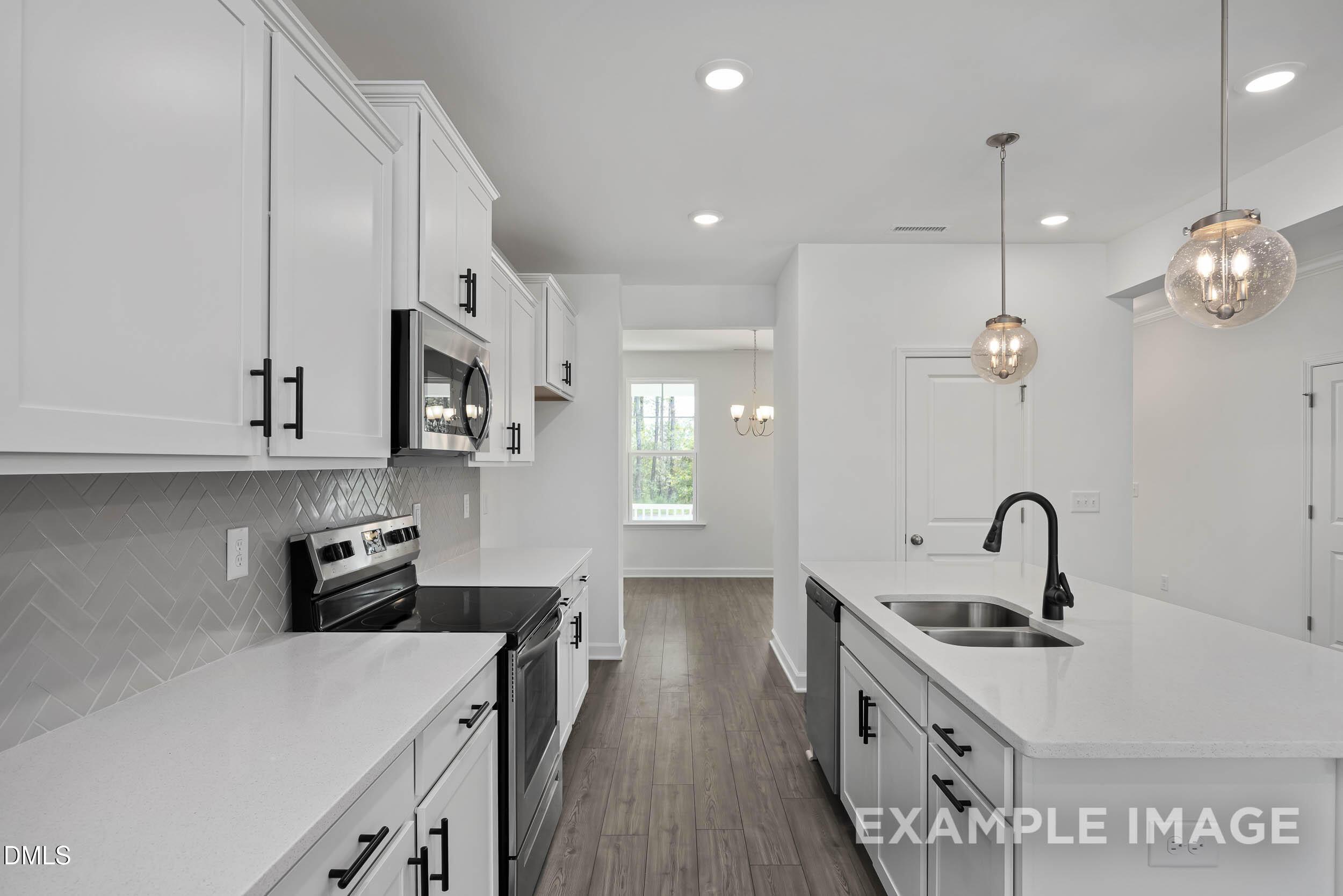 Modern white kitchen with subway tile backsplash, stainless appliances, and quartz island in The Willow D by Davidson Homes, Zebulon, NC
