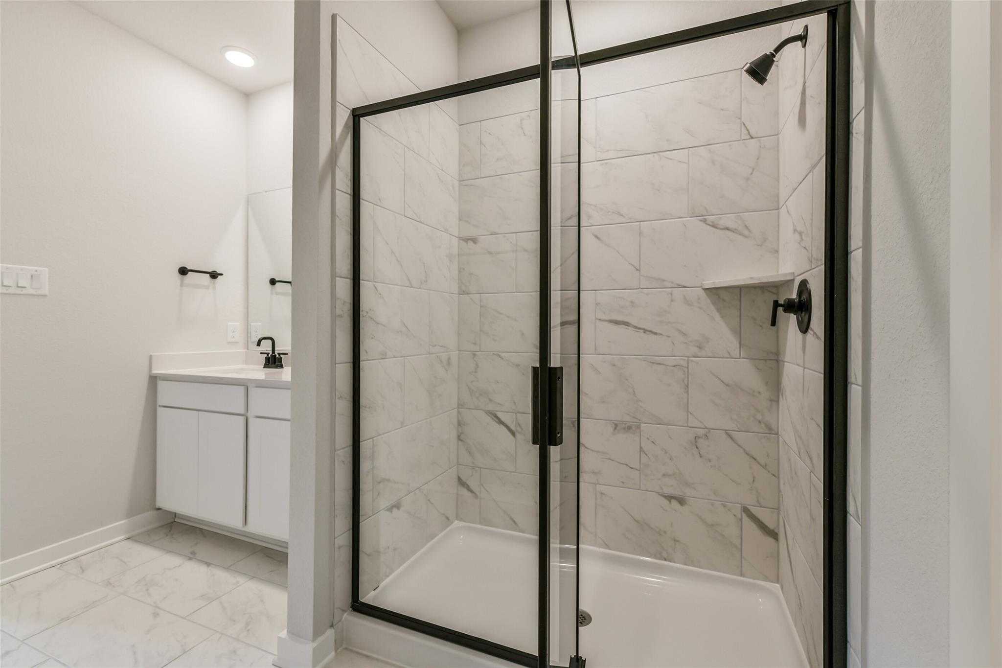 Elegant master bathroom with frameless glass shower, white subway tile, and single vanity in Davidson Homes The Daphne H, Crosby Texas