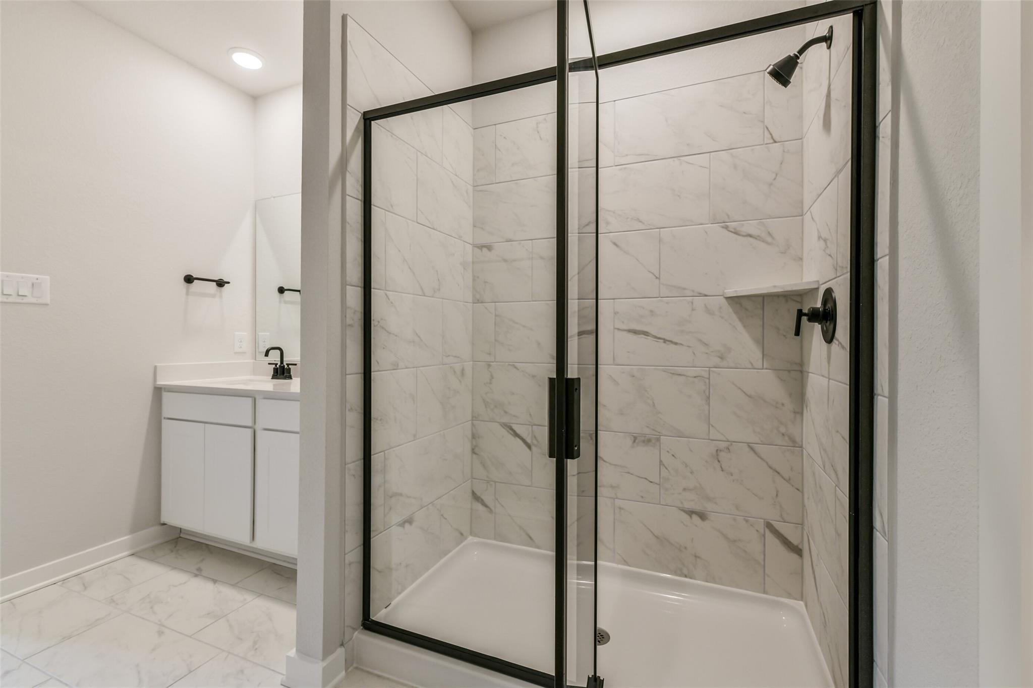 Elegant master bathroom with frameless glass shower, white subway tile, and single vanity in Davidson Homes The Daphne H, Crosby Texas
