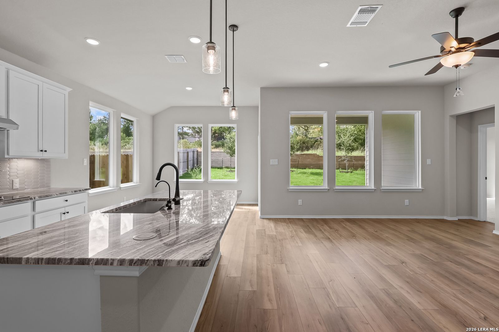 Open-concept kitchen with granite island, white cabinetry, and pendant lights in Davidson Homes The Sequoia C, San Antonio, Texas