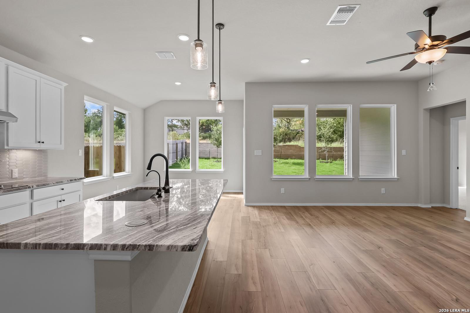 Open-concept kitchen with granite island, white cabinets, and hardwood floors in Davidson Homes The Sequoia C at Royal Crest, San Antonio