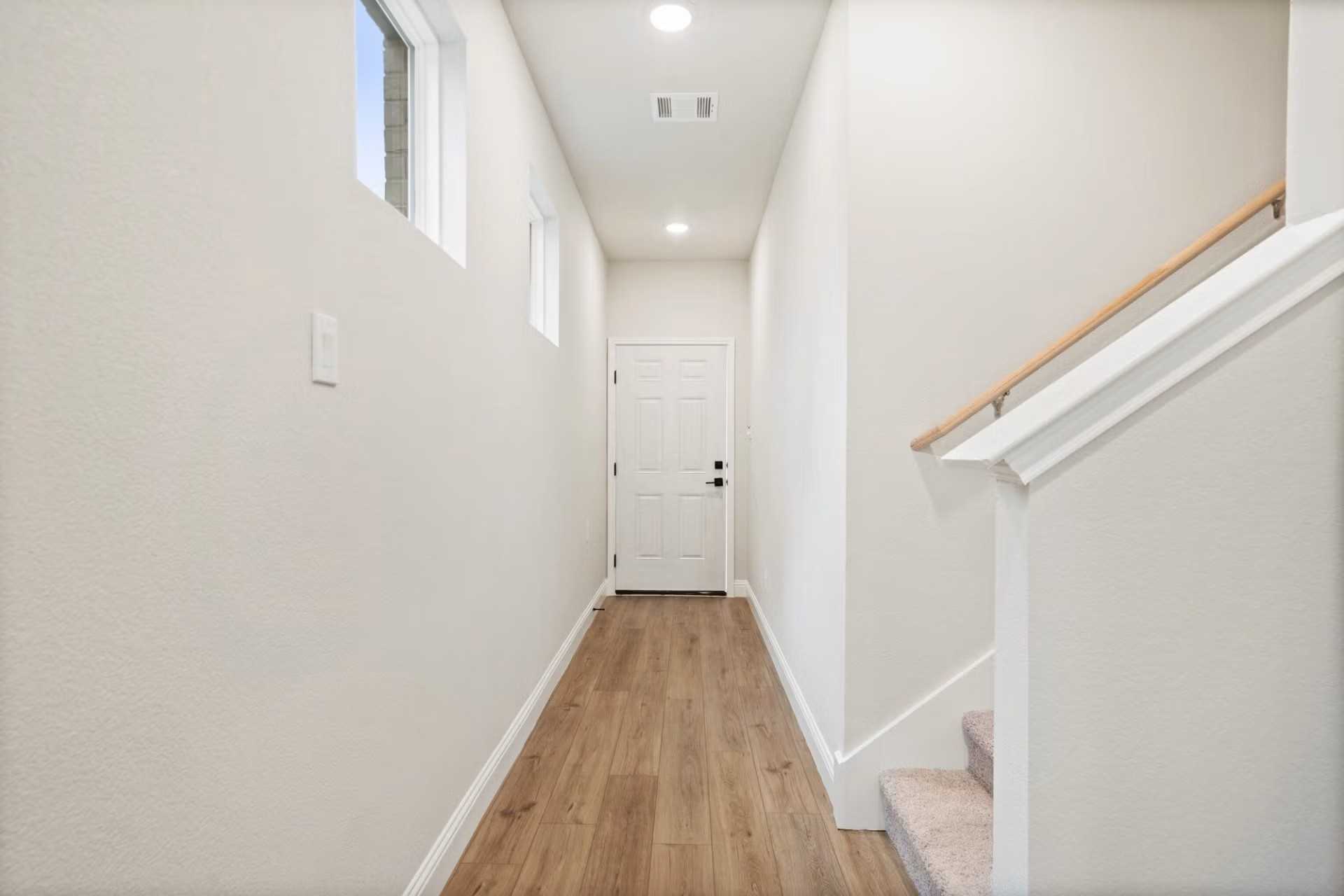 Bright hallway with hardwood floors, white walls, and staircase in Davidson Homes The Wake D, Wylie Texas