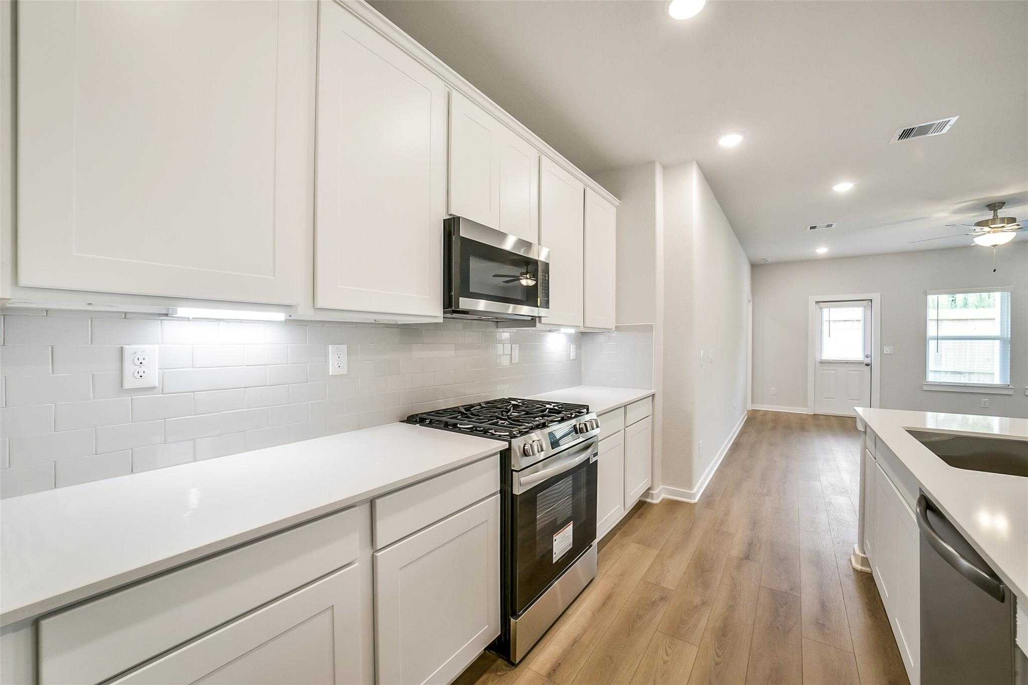 Modern white kitchen with stainless steel appliances, quartz counters, and subway tile backsplash in Davidson Homes The Blanco E, Magnolia TX
