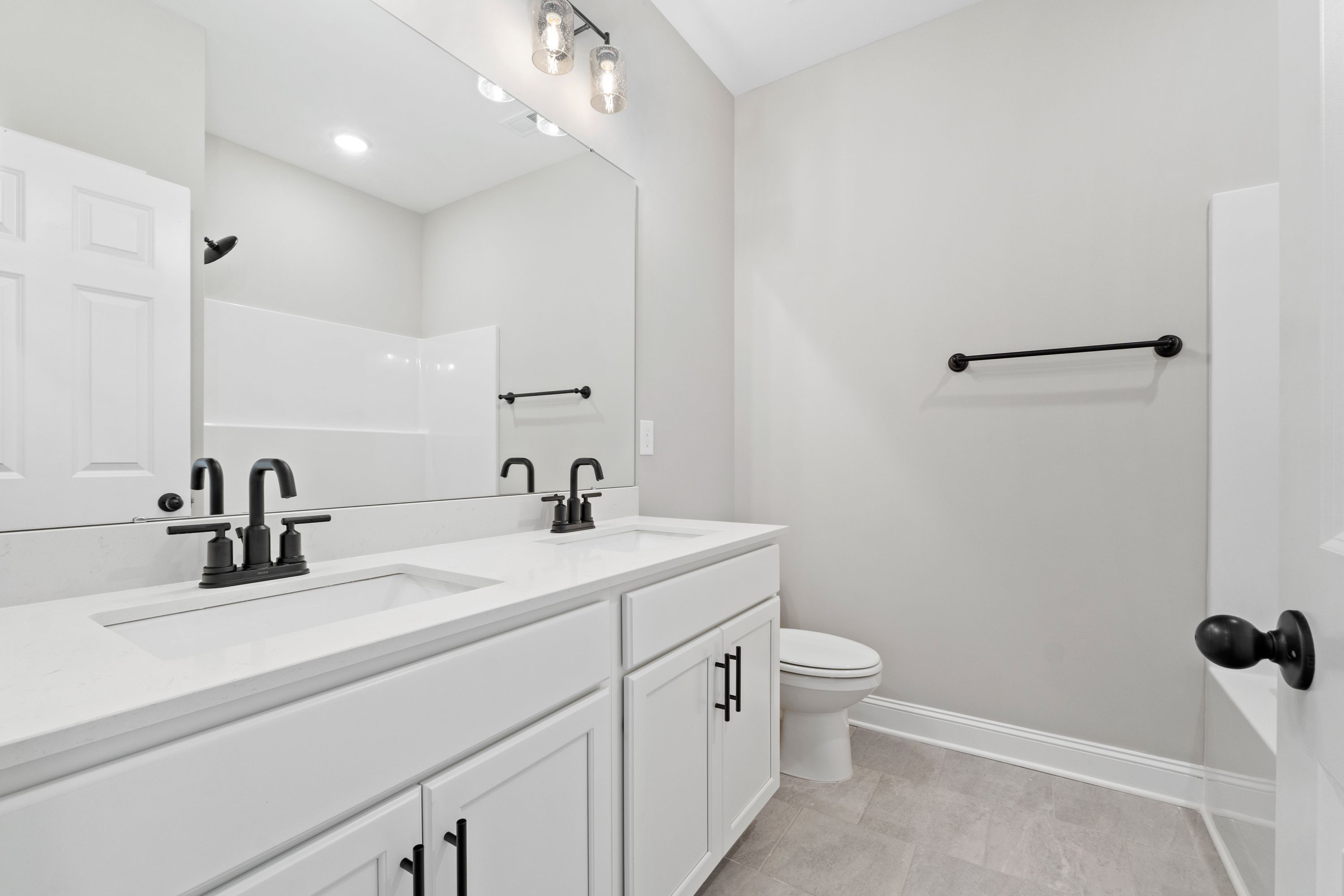 Spacious master bathroom in The Valencia with double vanity, black faucets, frameless shower, and gray walls
