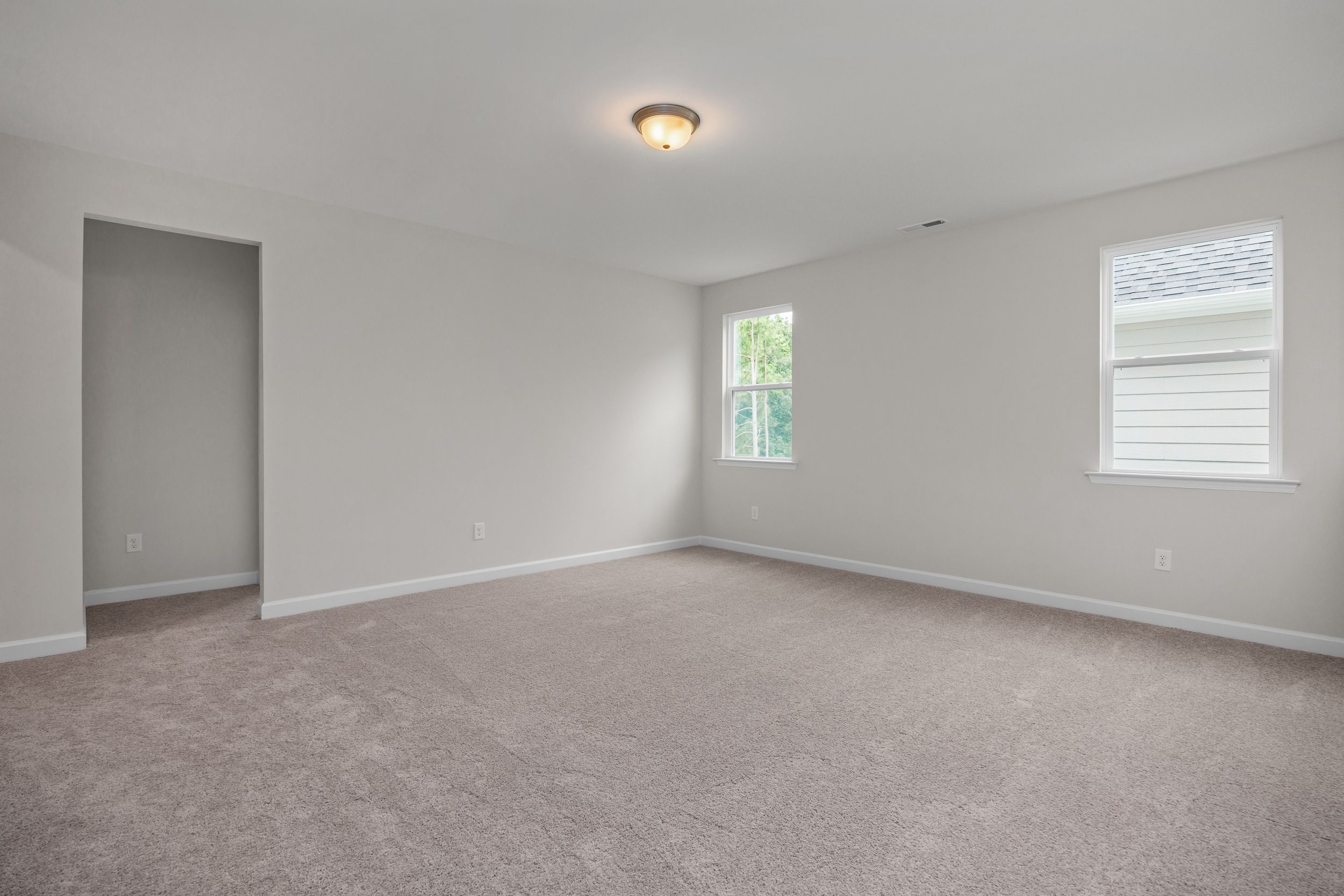 Spacious upstairs bedroom in The Aspen home design with neutral gray walls, beige carpet, double windows, and closet doorway