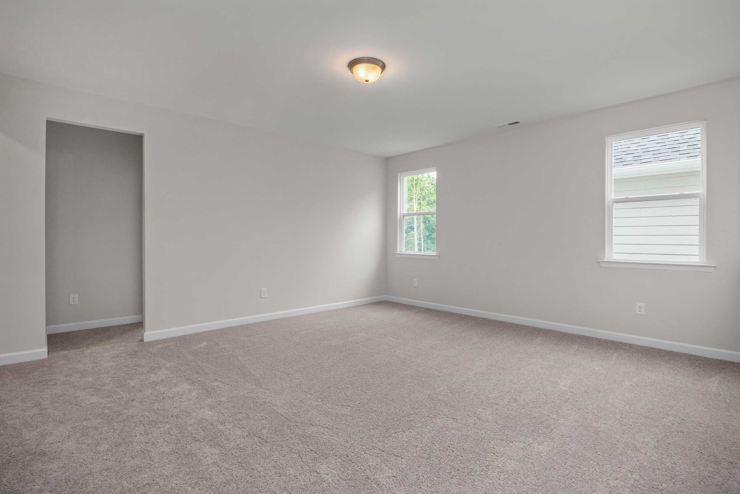 Spacious upstairs bedroom in The Aspen home design with neutral gray walls, beige carpet, double windows, and closet doorway