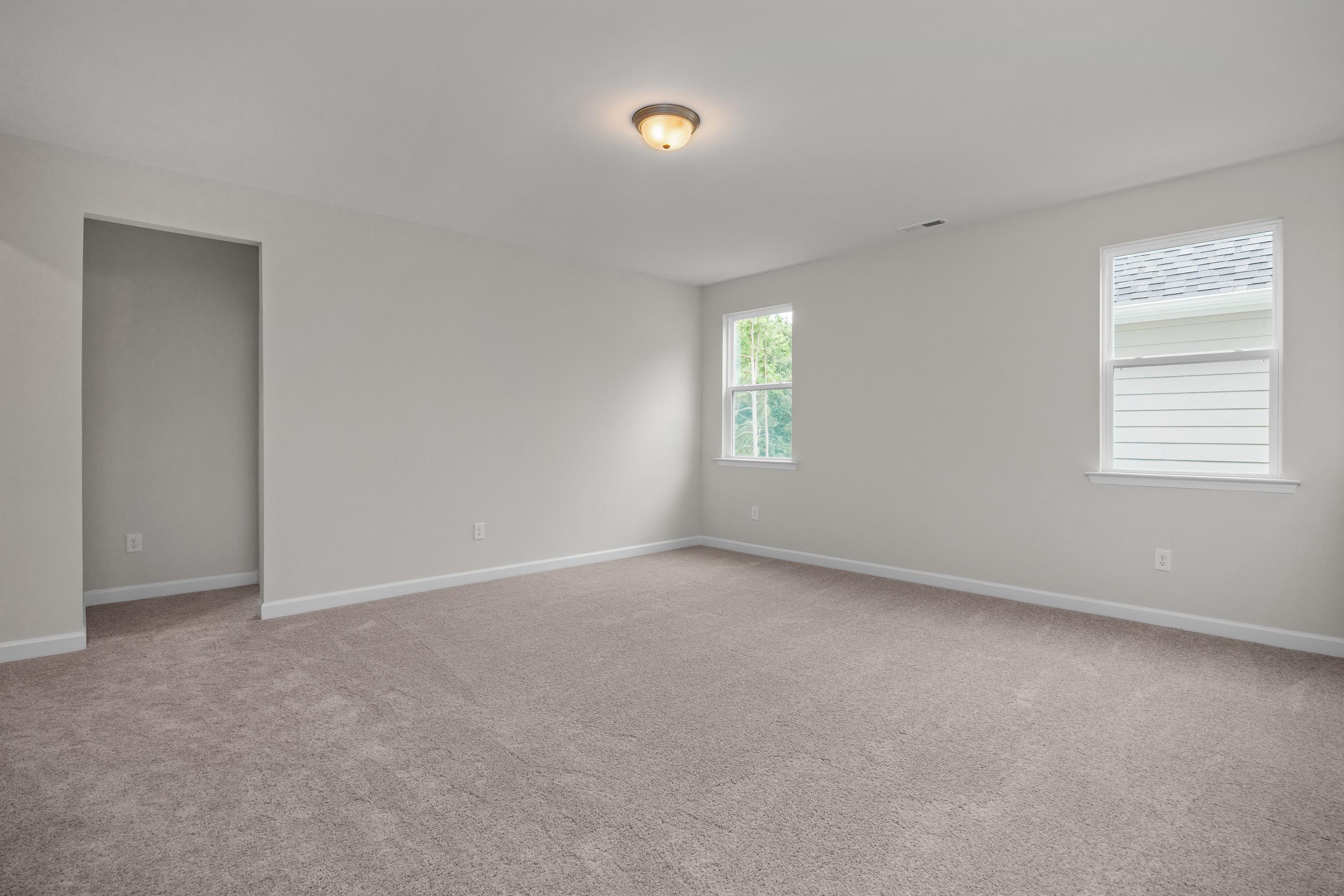Spacious upstairs bedroom in The Aspen home design with neutral gray walls, beige carpet, double windows, and closet doorway