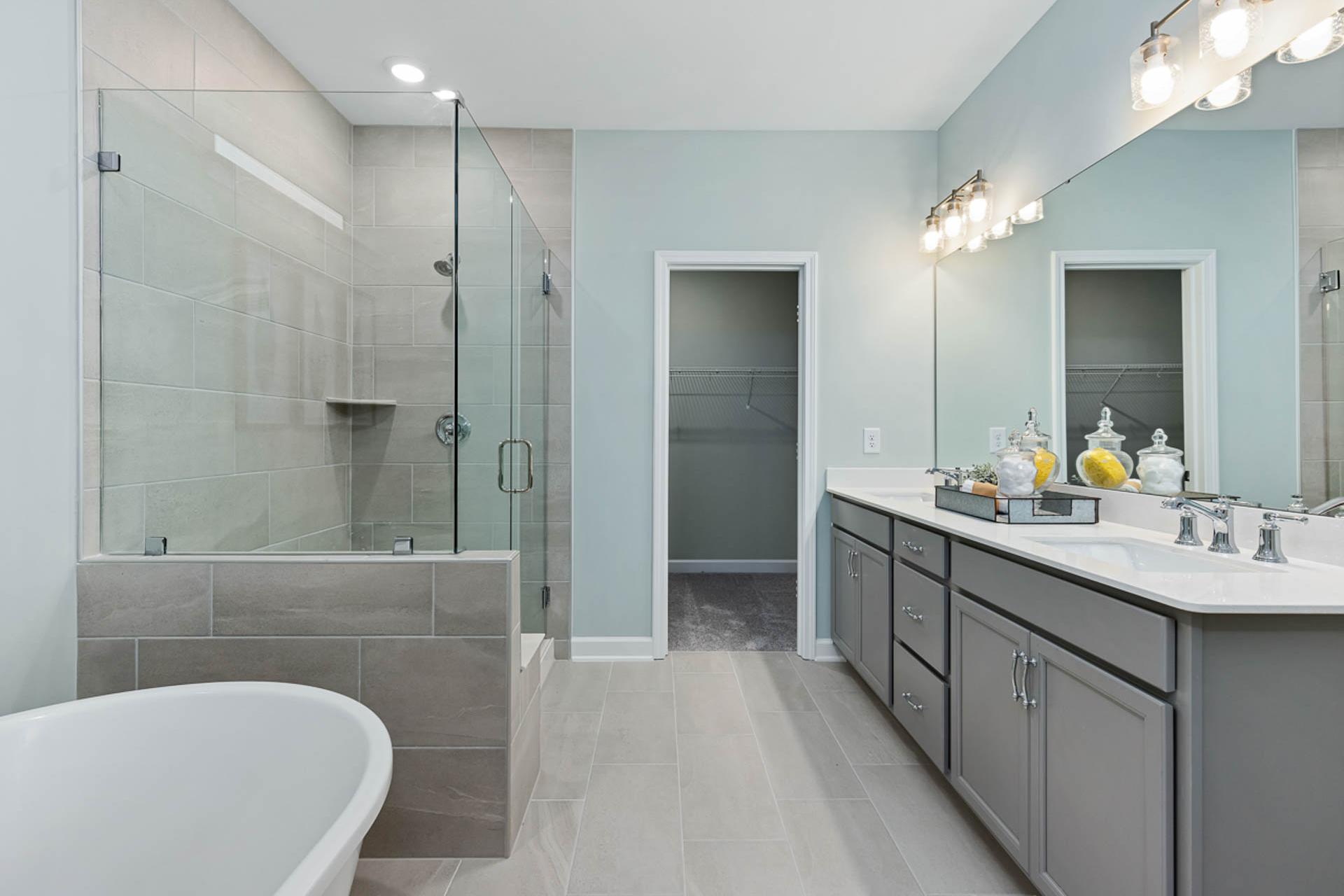 Spacious master bath at Weatherford East in Angier NC with glass shower, freestanding tub, double vanity, and soft blue walls