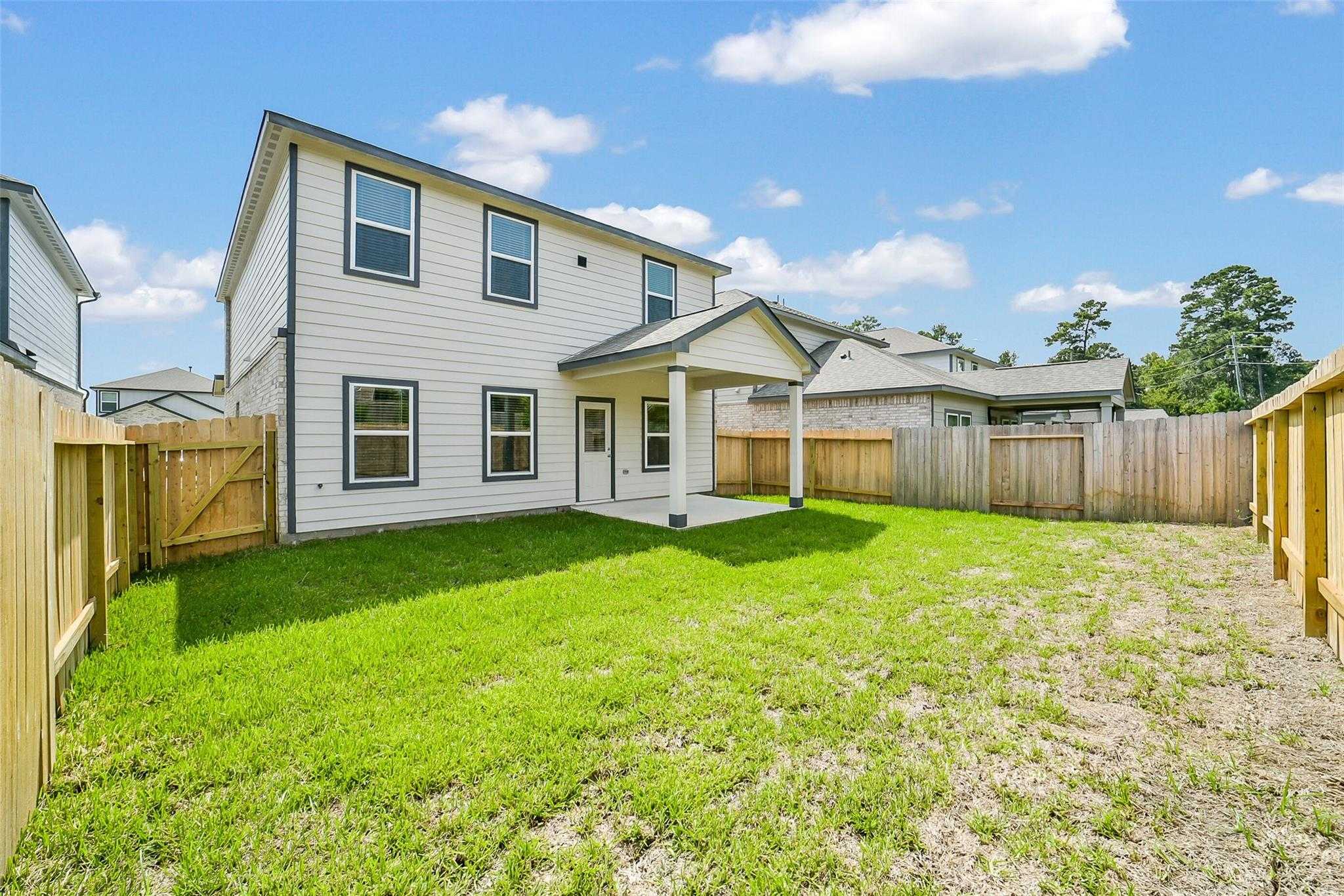 Two-story white home exterior with covered back patio, fenced green lawn, and blue sky in Lakes at Black Oak, Magnolia, Texas - Davidson Homes The Trinity F