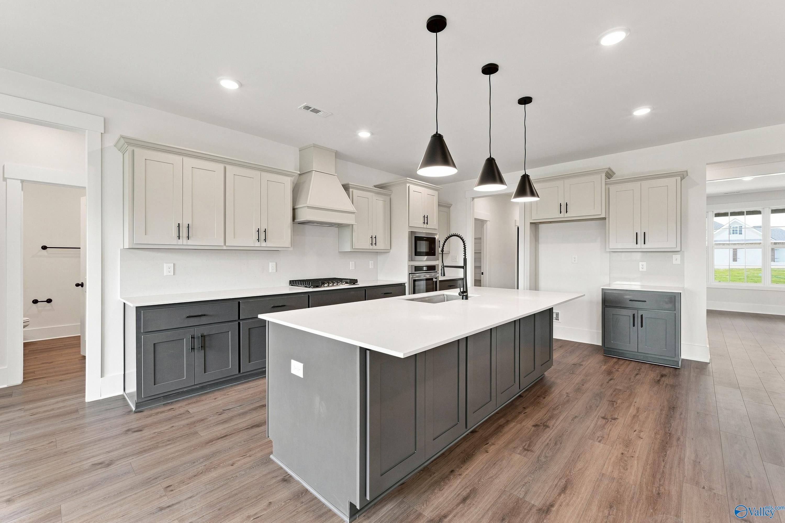 Modern kitchen with large gray island, white quartz countertops, black pendant lights, and hardwood floors in Davidson Homes' The Valencia, Huntsville, Alabama