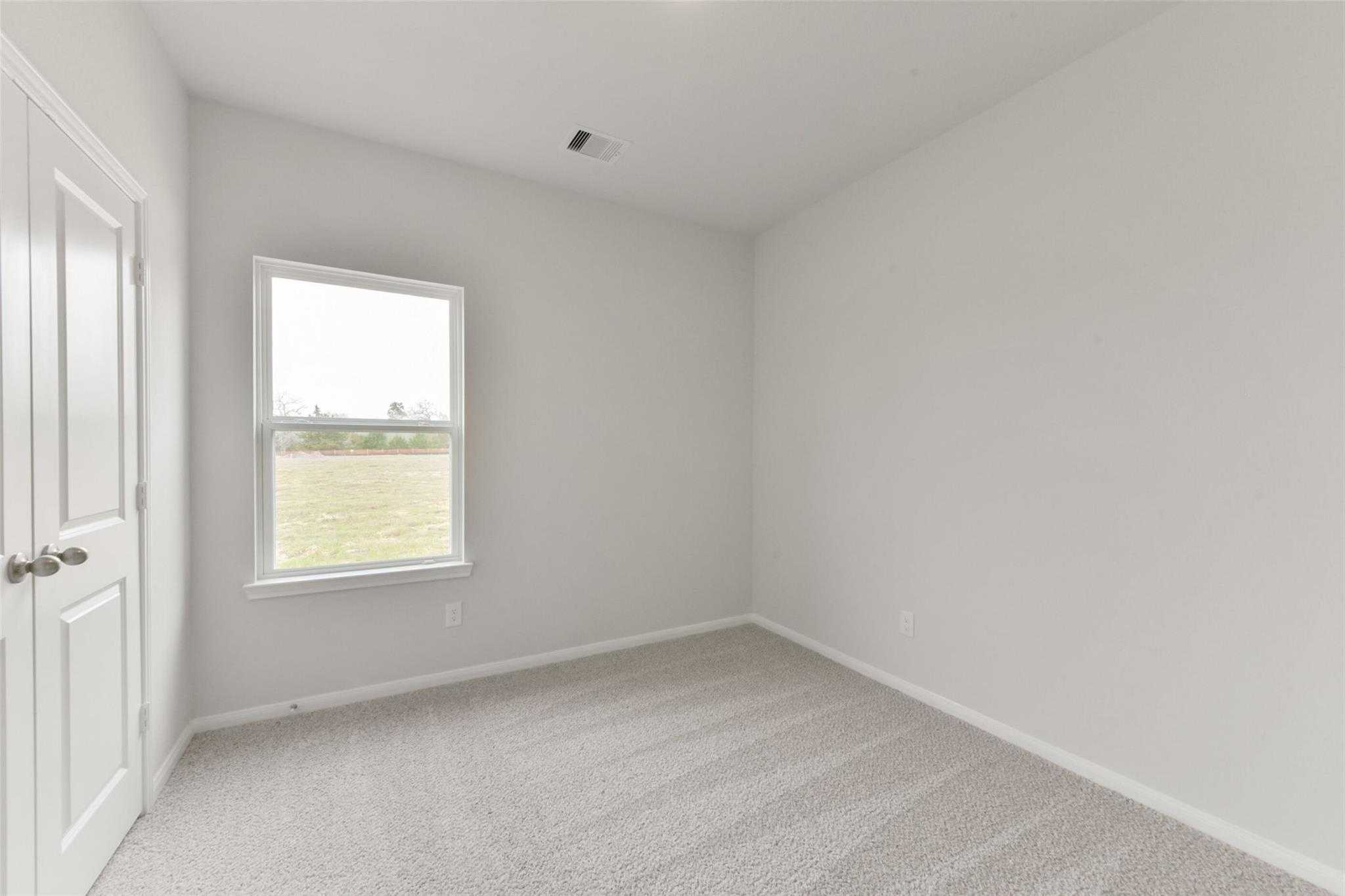 Empty secondary bedroom with beige carpet, white walls, and window overlooking green field in Davidson Homes The Laguna B, Magnolia TX