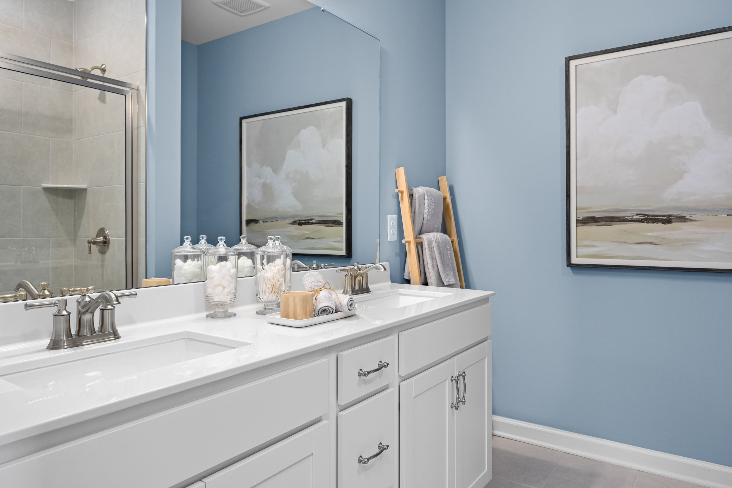 Spacious master bathroom in The Magnolia B featuring blue walls, double vanity, glass shower, and abstract art