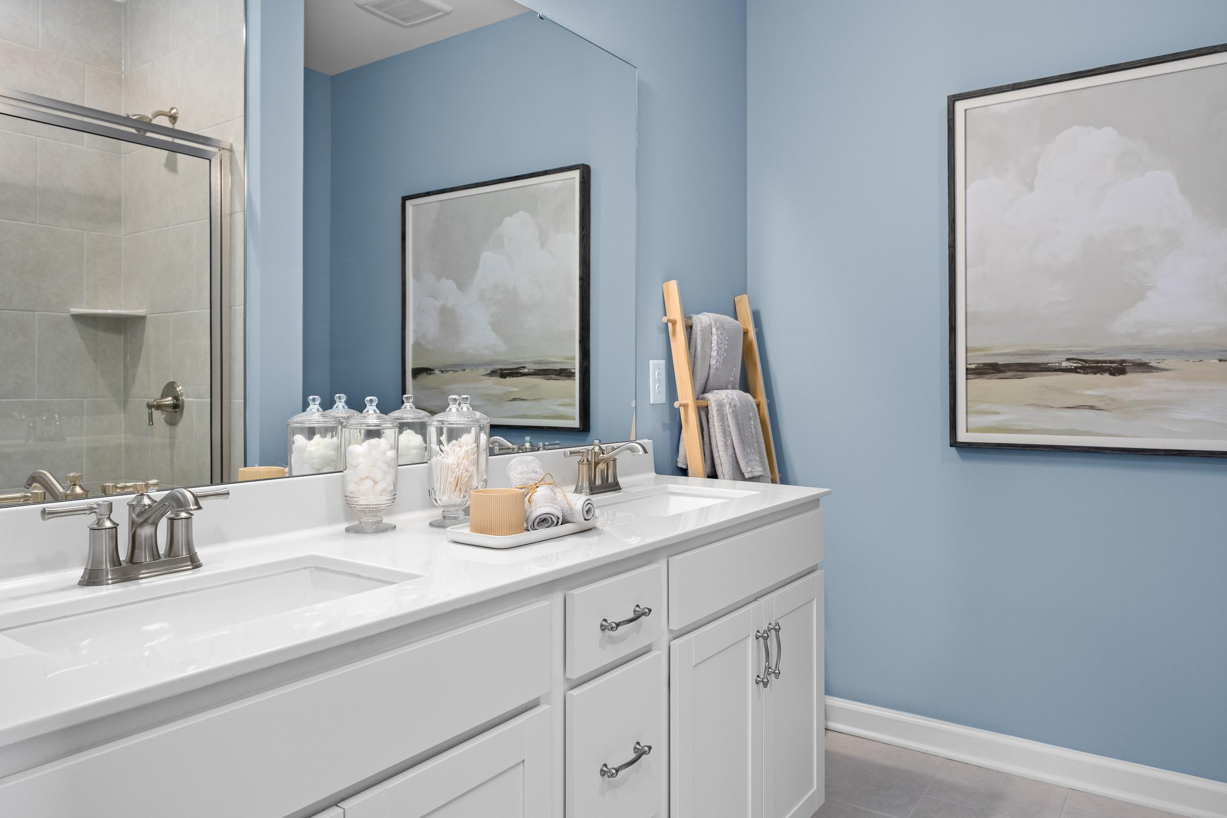 Modern master bathroom in The Magnolia A with blue walls, double vanity, frameless shower, and abstract art