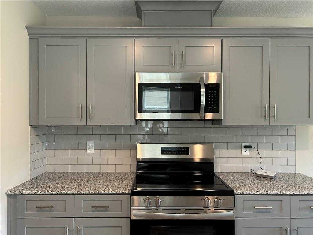 Modern kitchen with gray shaker cabinets, stainless steel appliances, granite countertops, subway tile backsplash in Davidson Homes The Washington, Phenix City